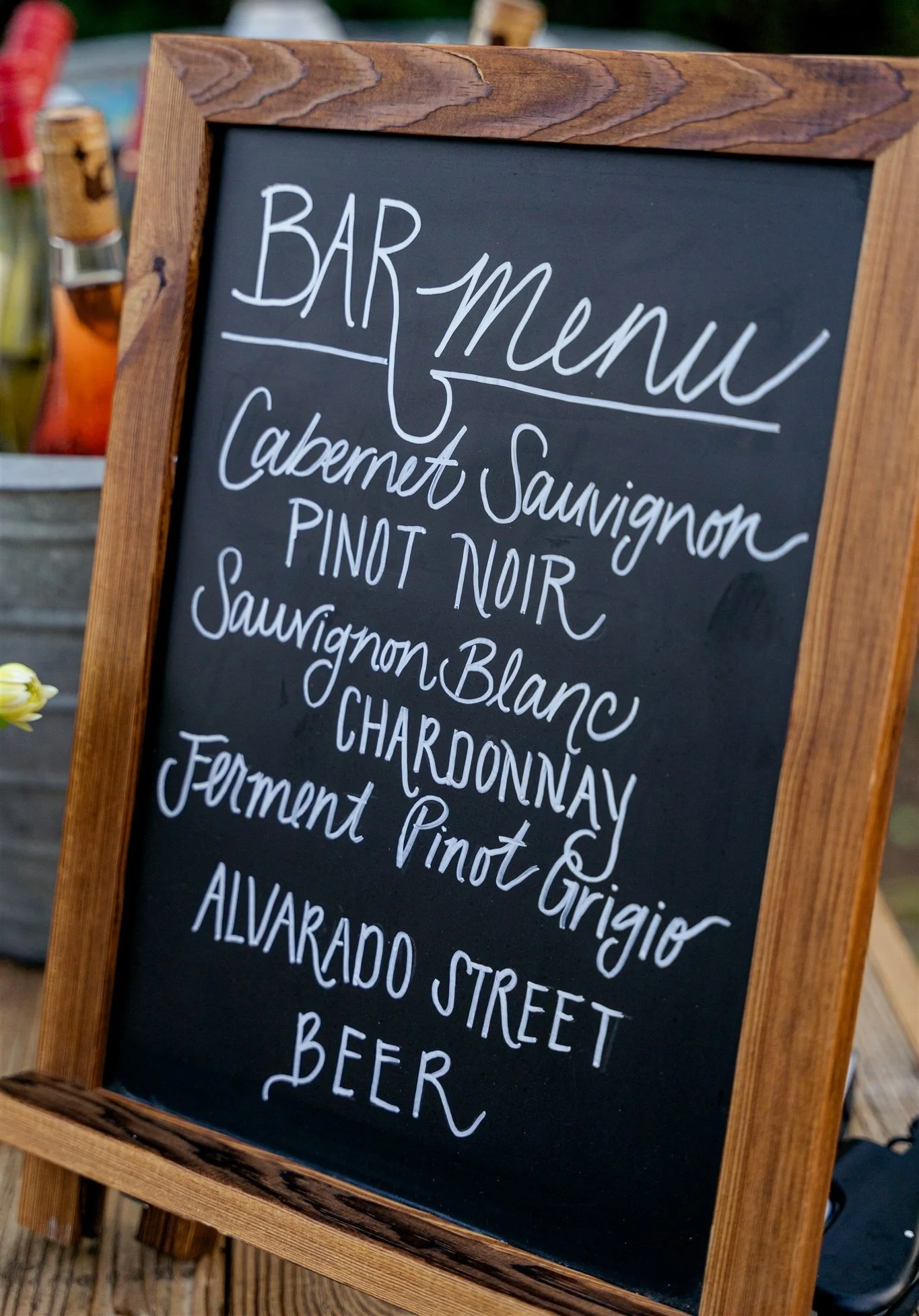 A wooden-framed chalkboard sign labeled “Bar Menu” lists wines including Cabernet Sauvignon, Pinot Noir, Sauvignon Blanc, Chardonnay, Pinot Grigio, and beer.