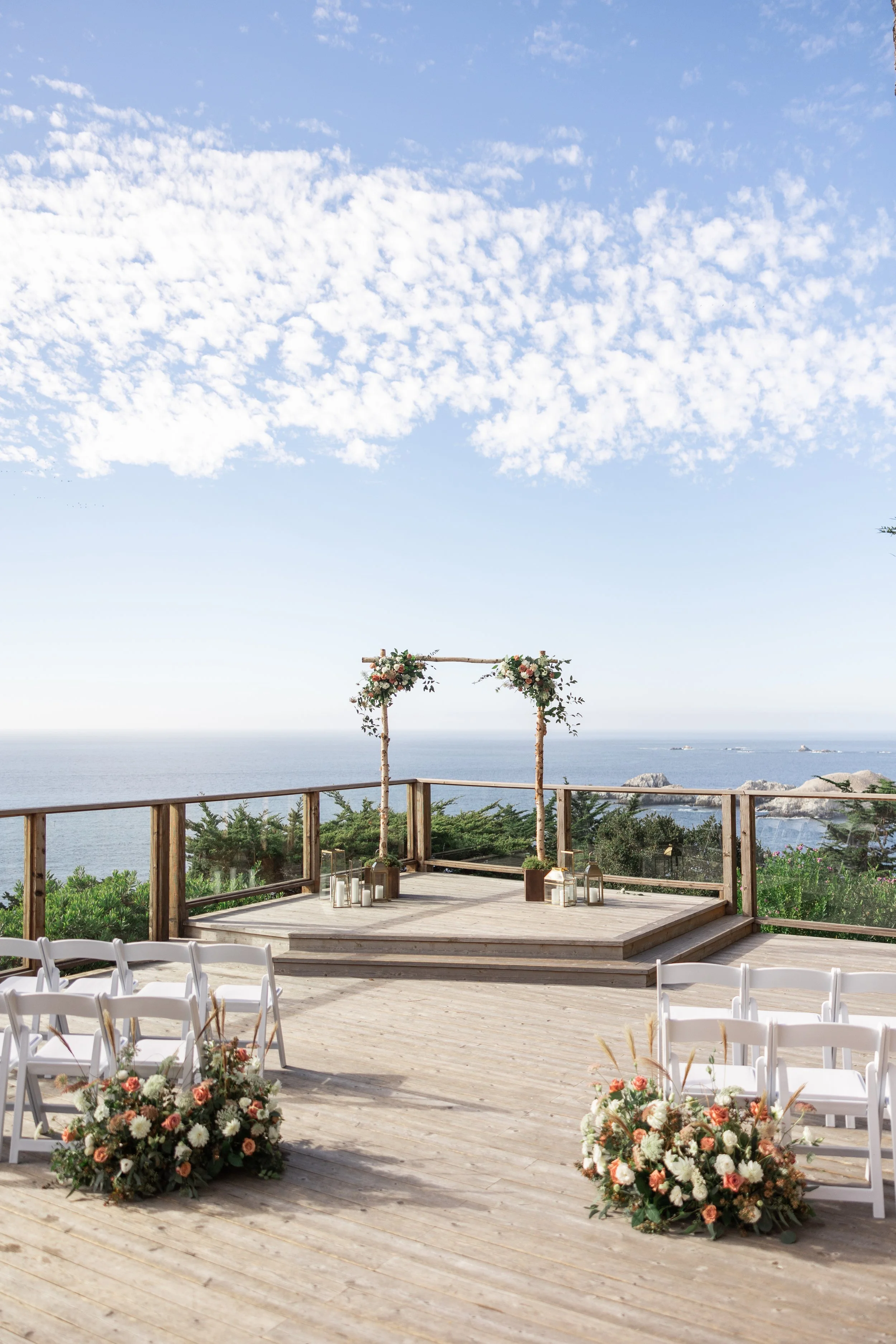 Coastal wedding ceremony setup with floral arrangements and a wooden arbor overlooking the Pacific Ocean
