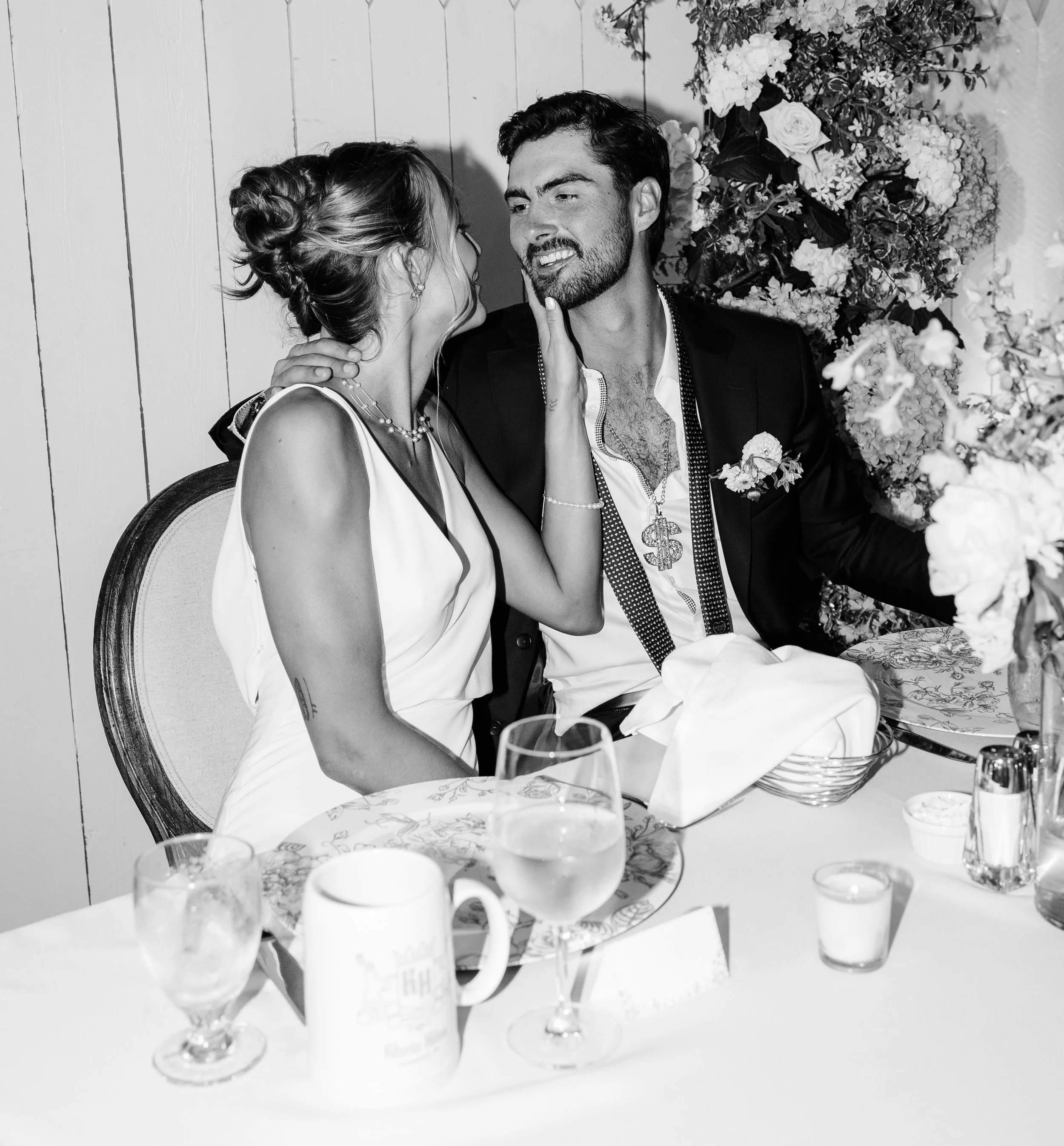 Bride and groom sharing a tender moment at their wedding reception sweetheart table, black and white photo.