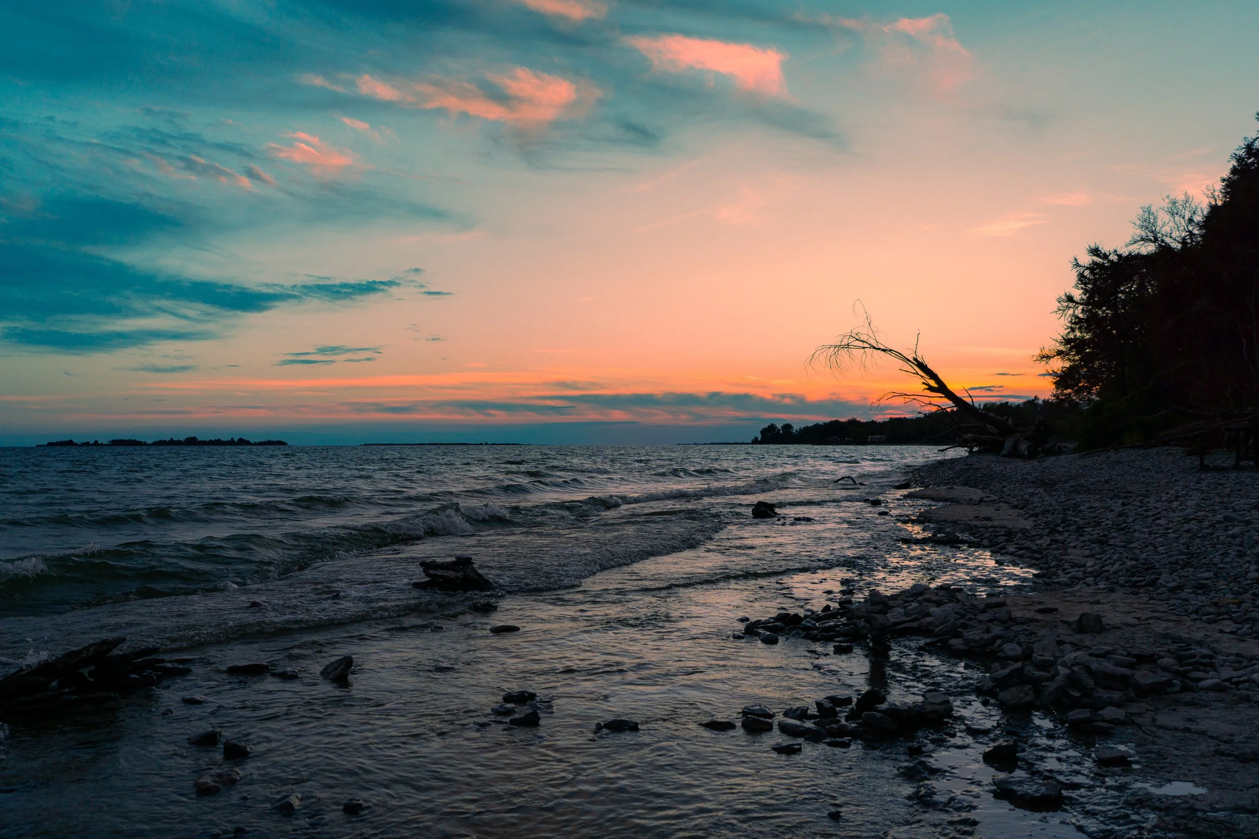 A scenic view of a sunset over a body of water, with colorful clouds in the sky and a silhouette of trees on the shoreline.