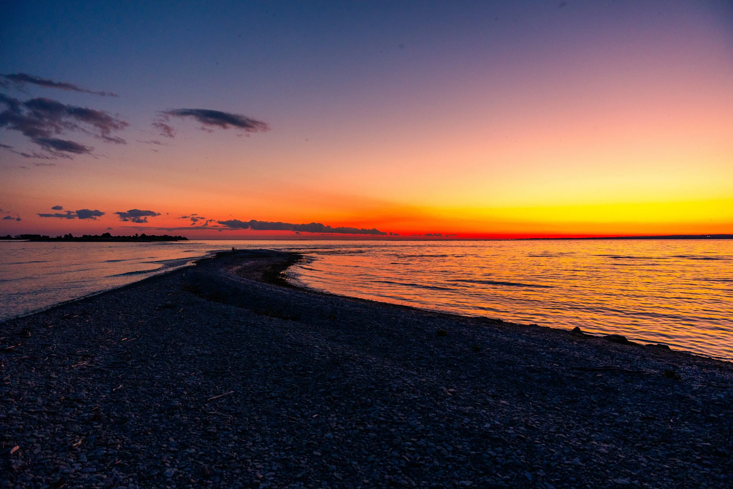 Sunset over a body of water with a small landmass in the distance and a partly cloudy sky.