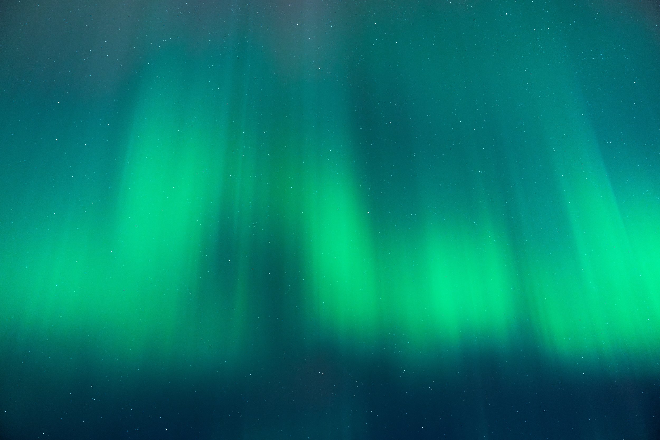 Photo of the night sky showing stars and the northern lights with green and blue hues.