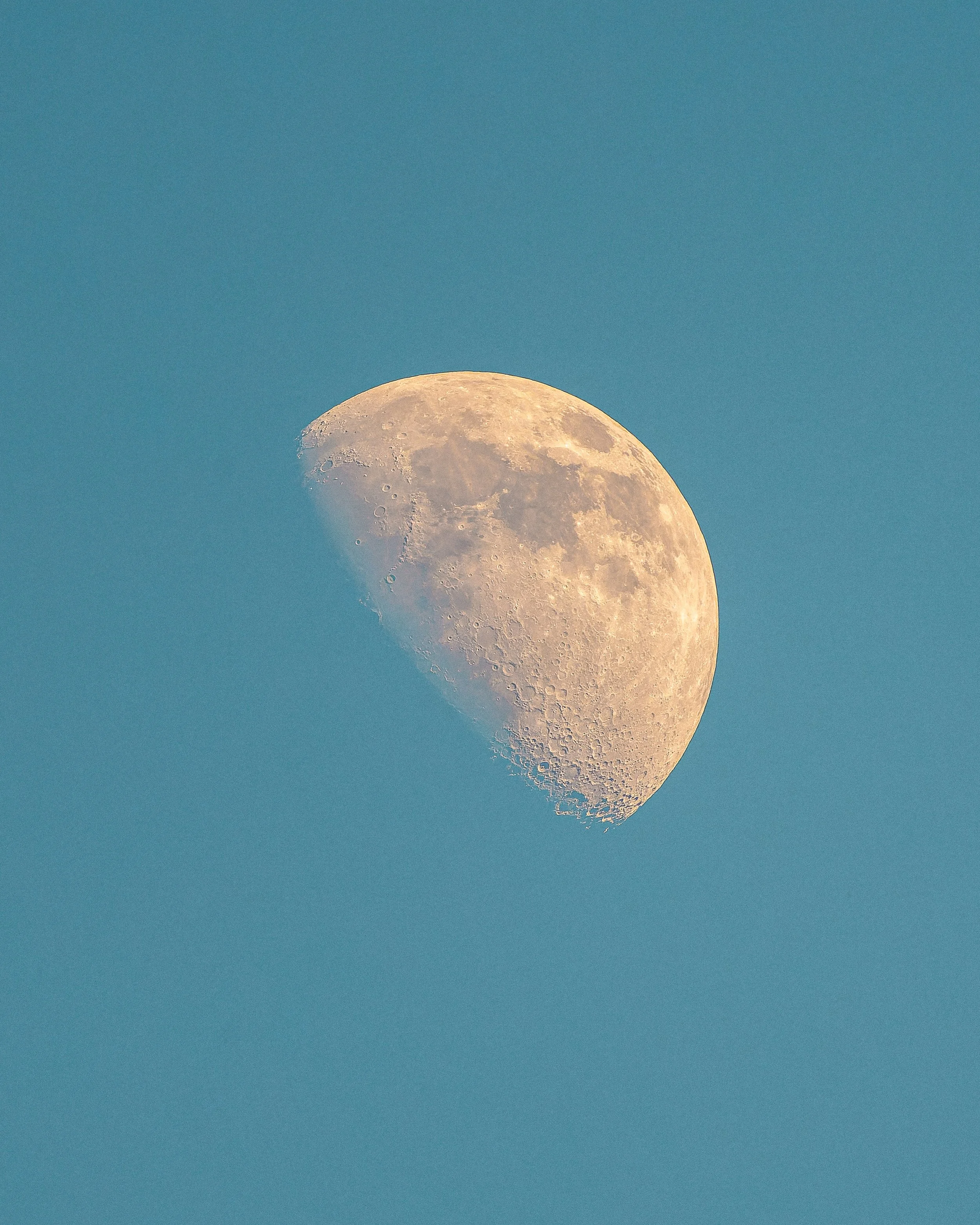 The moon with a portion of its surface illuminated, visible against a clear blue sky.
