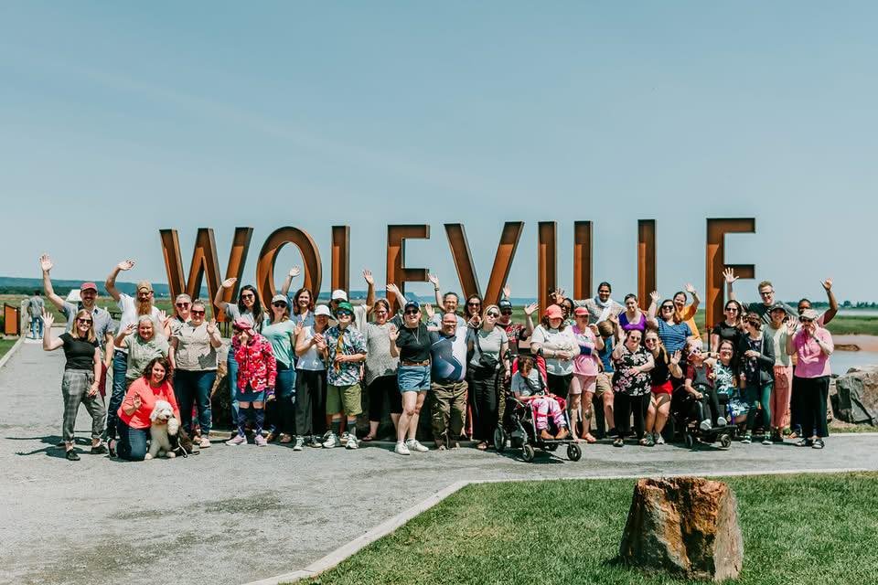 L'Arche Volunteers, Members and core members by the waterfront Wolfville sign