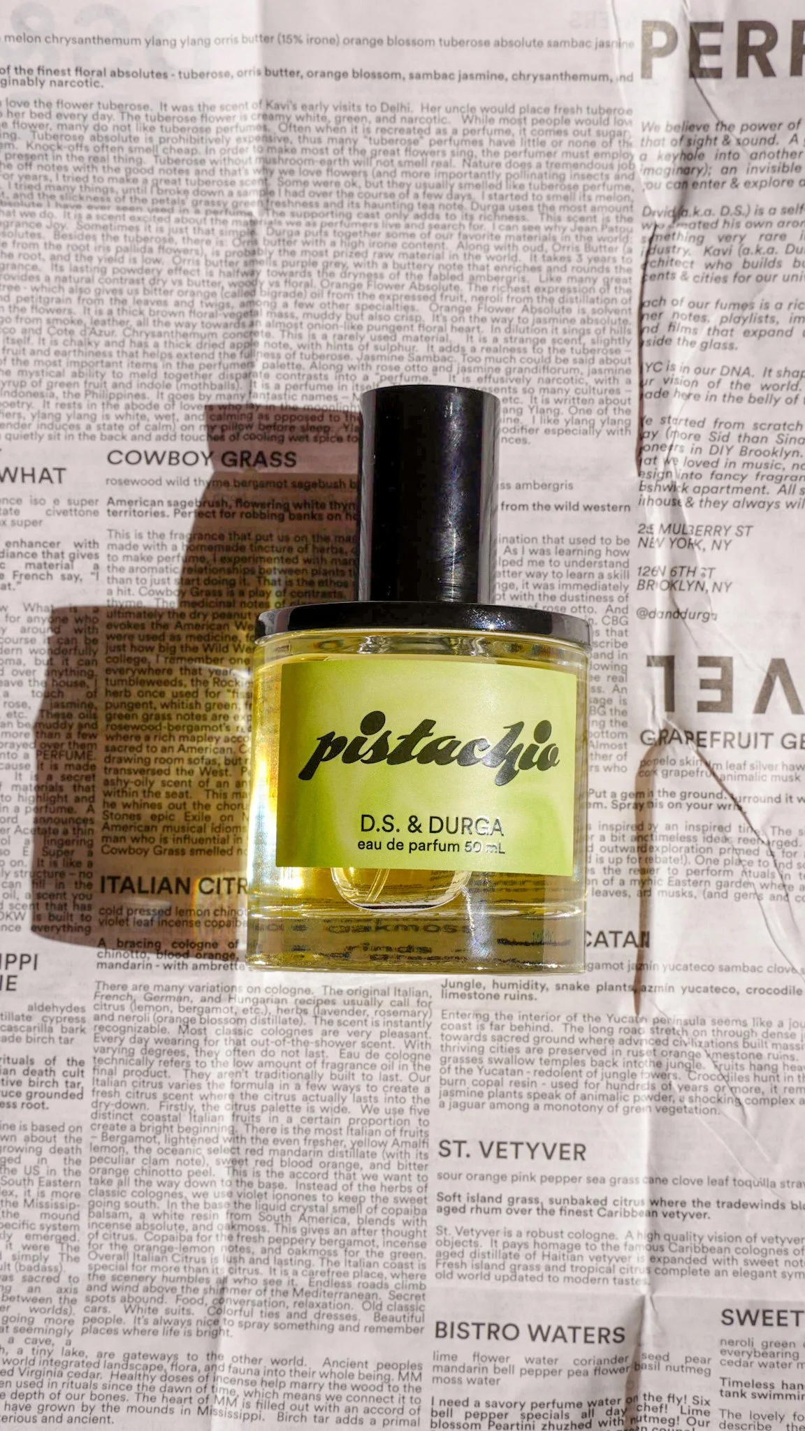 A small yellow perfume bottle labeled 'pistachio D.S. & DURGA eau de parfum 50 mL' placed on a newspaper background.