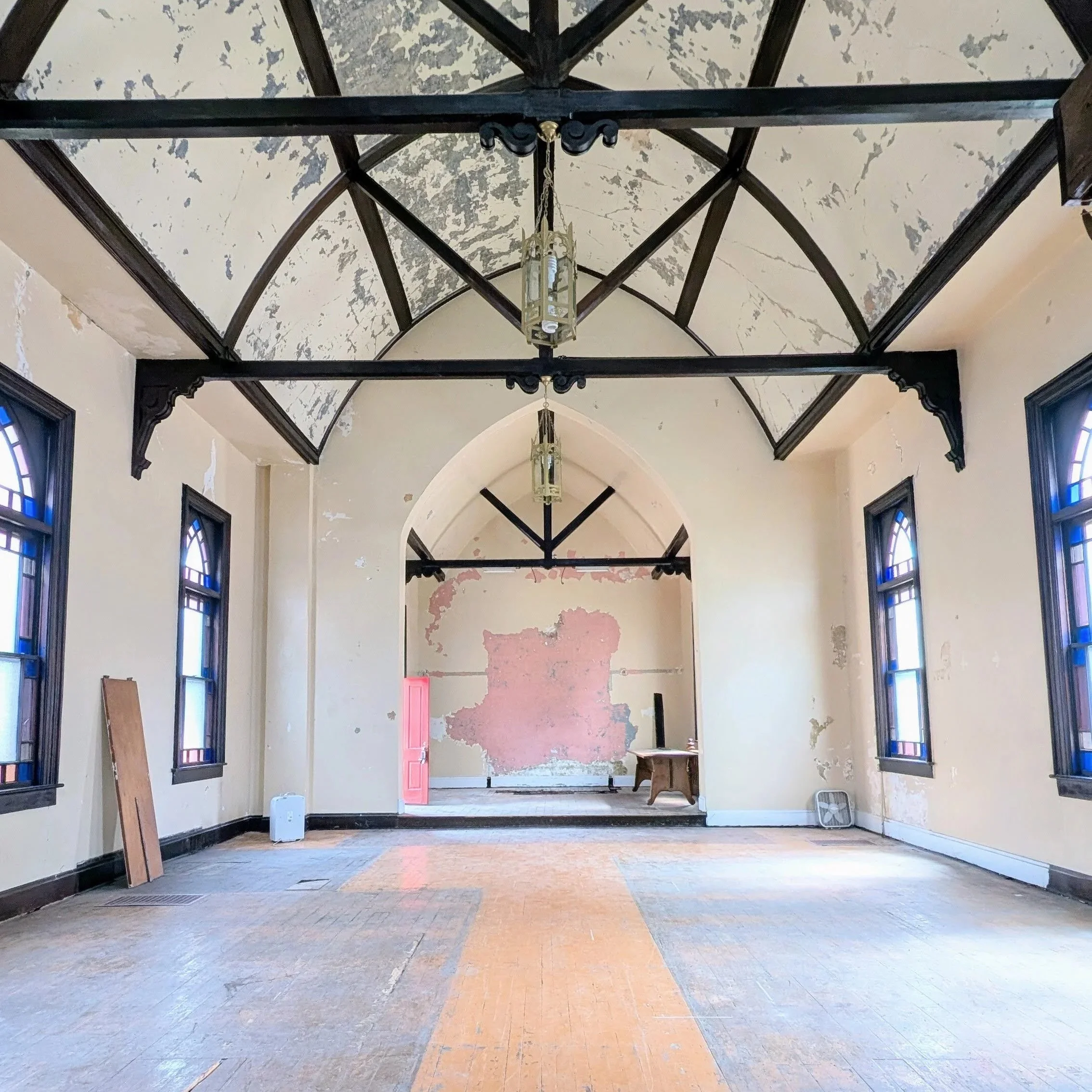A cozy rendering of updated Lille Bønne interior with various seating arrangements including sofas and chairs, a small table with a chessboard, a dining table with chairs, bookshelves, and decorative stained glass windows.