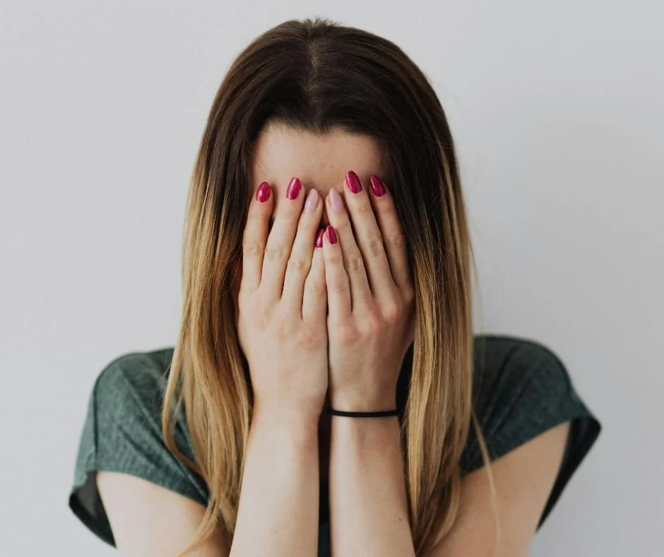 woman with head in hands upset with pink and red nail polish on