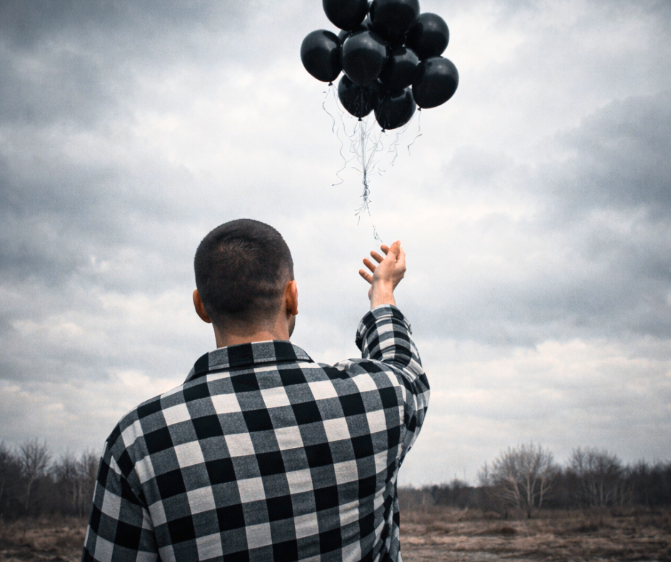 man in black and white flannel letting go of bouquet of black balloons