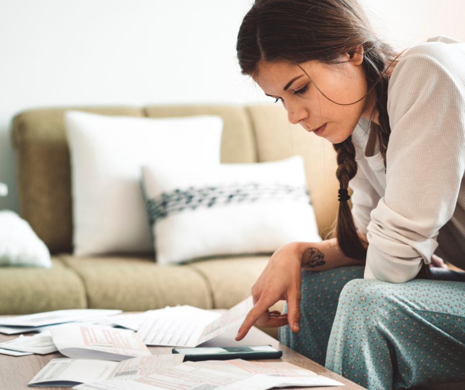 young woman sitting on edge of couch looking at phone and paper on end table