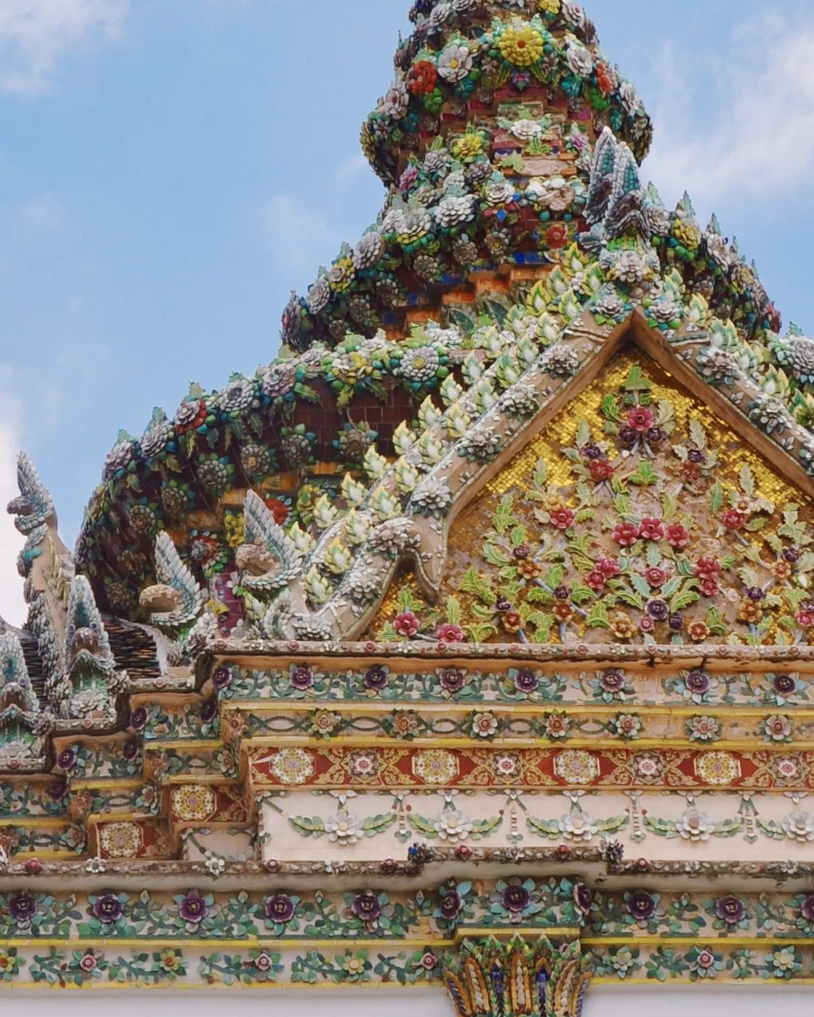 Close-up of ornate, colorful temple roof decorated with floral ceramic tiles and sculptures, set against a blue sky