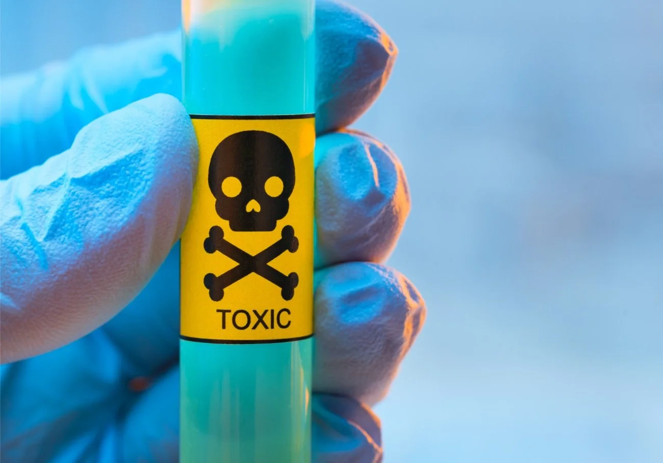 A hand in a blue glove holding a laboratory vial with a toxic warning sticker