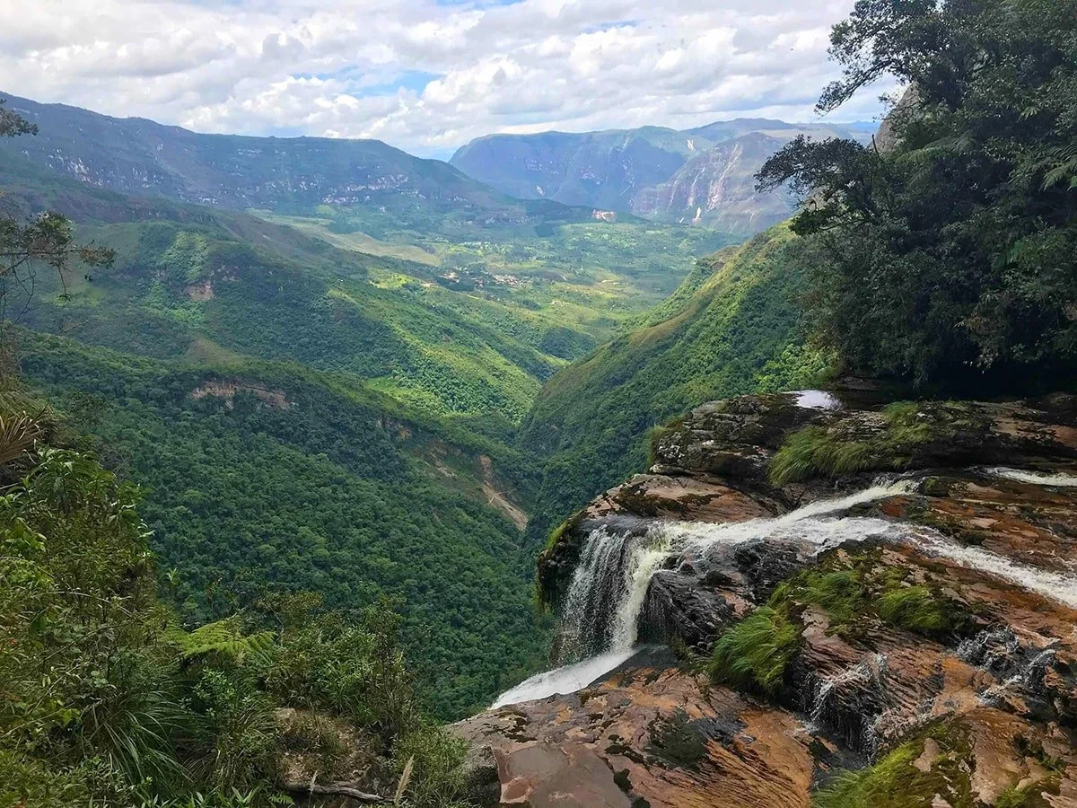 A waterfall in front of a lush and mountainous countryside