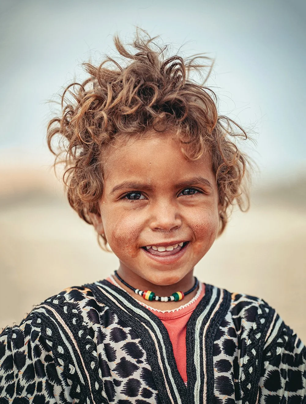 A smiling child with curly hair and a colorful neckless