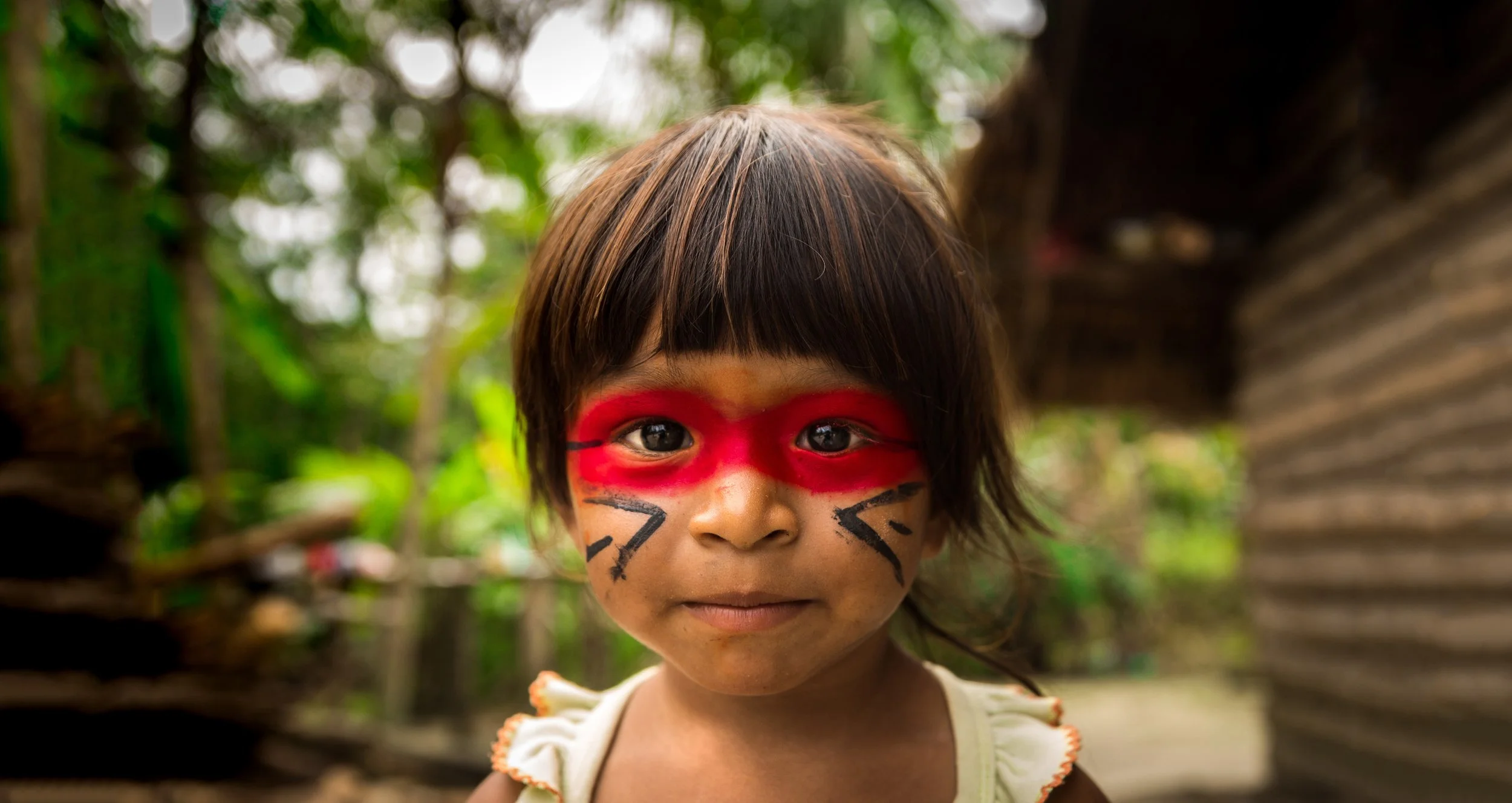 An indigenous child with red paint around her eyes