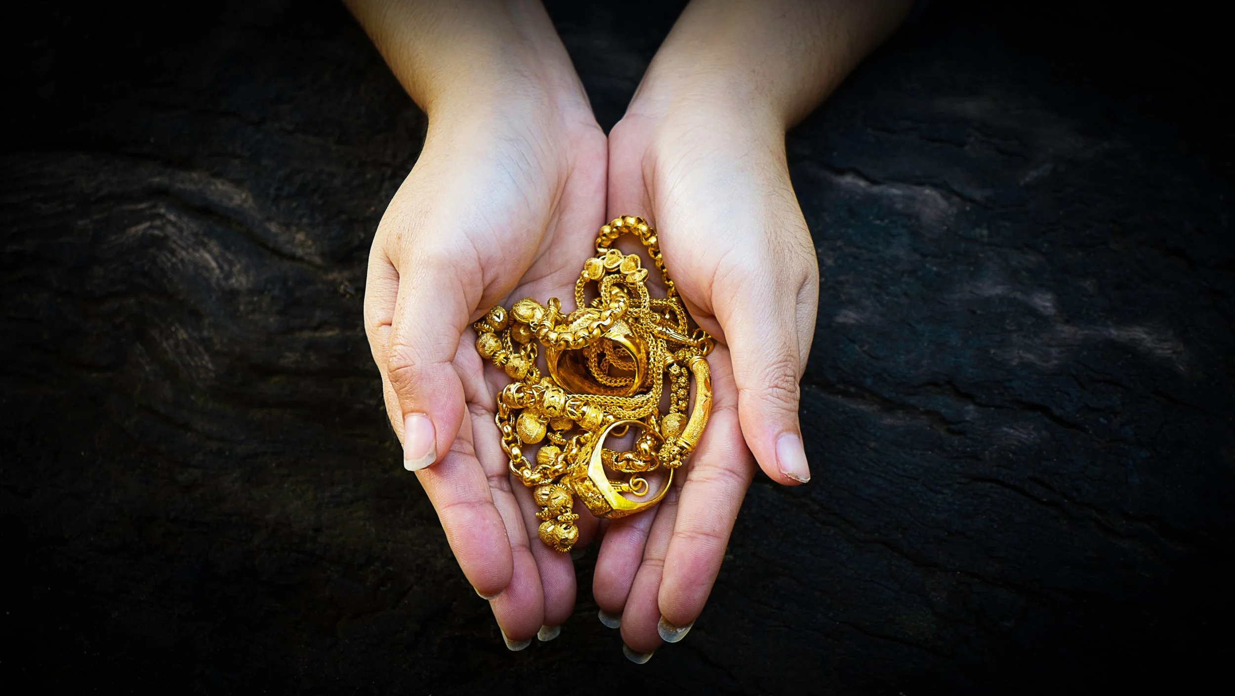 Two hands holding different pieces of gold jewelry