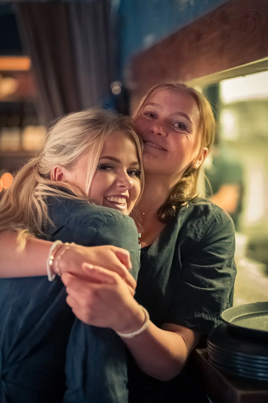 Två kvinnor som kramas och ler, inomhusmiljö, festlig stämning.