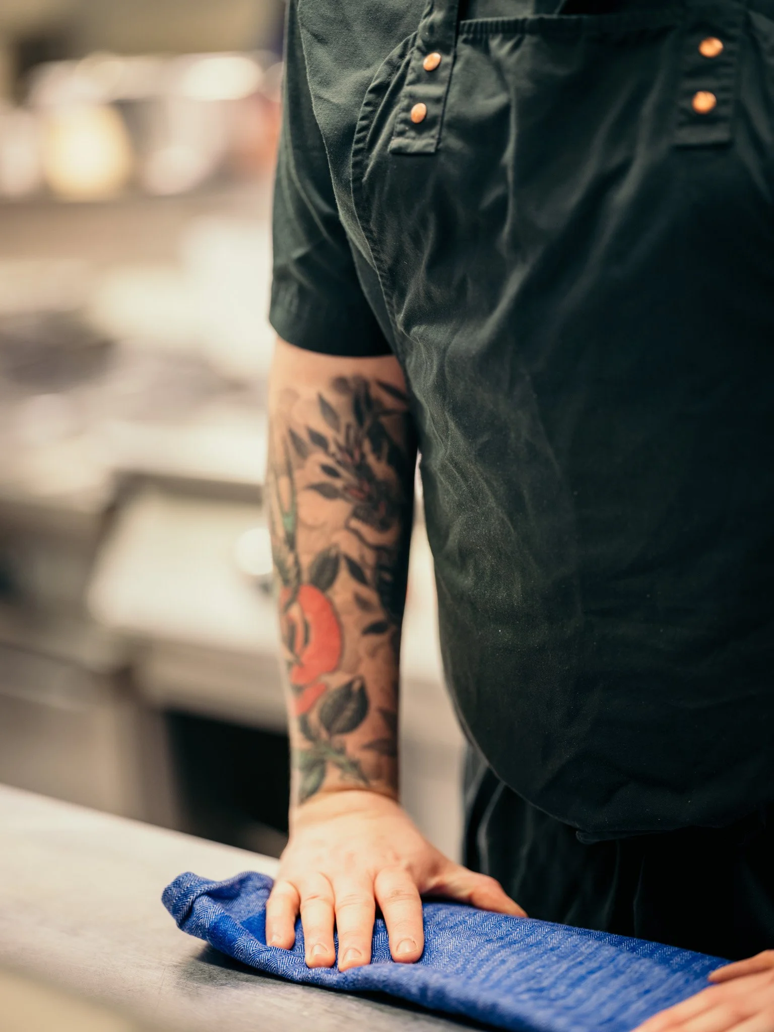 Kock med tatuerade armar står i köket.