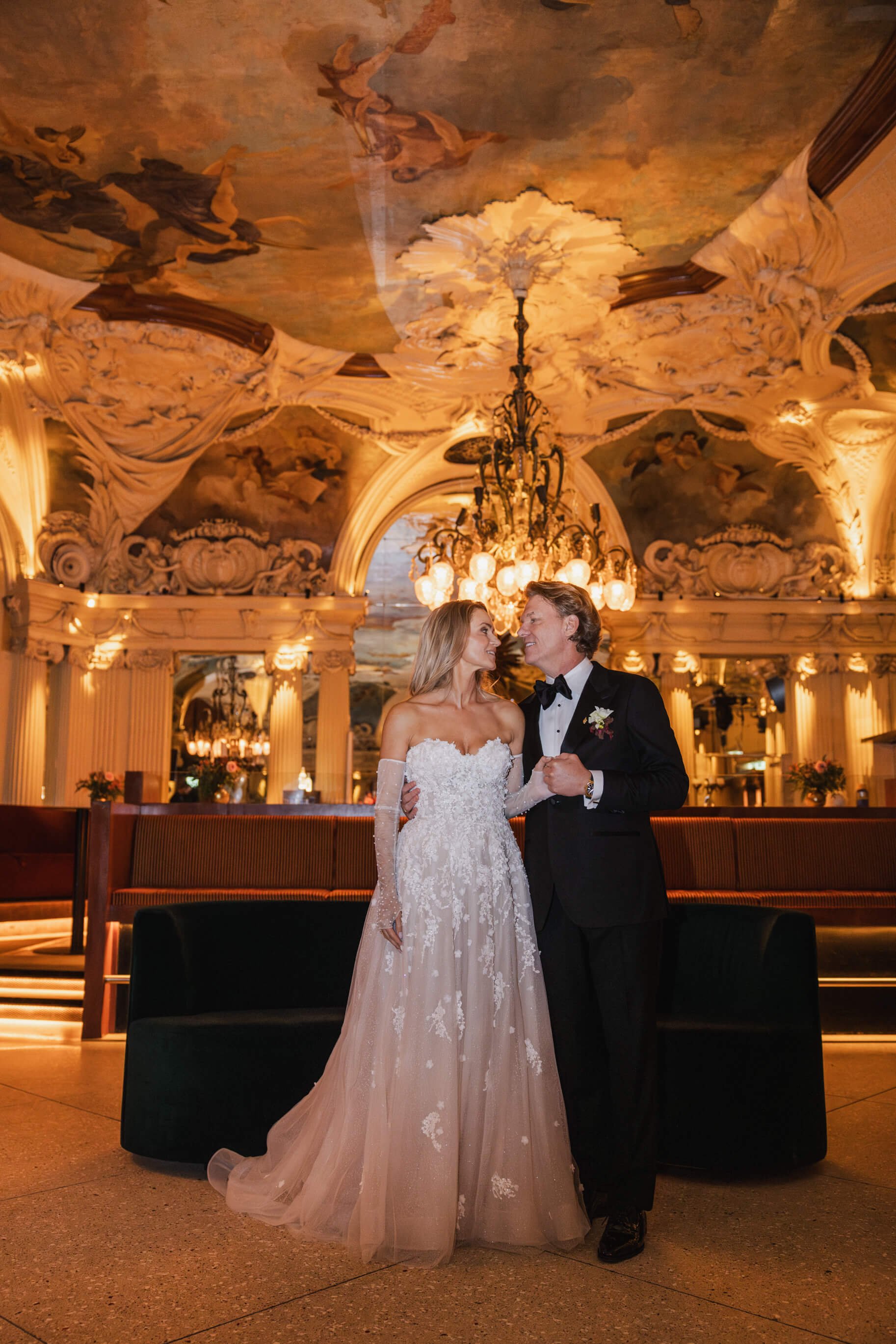 Full-length wedding portrait of a couple beneath a chandelier at Café Opera Stockholm