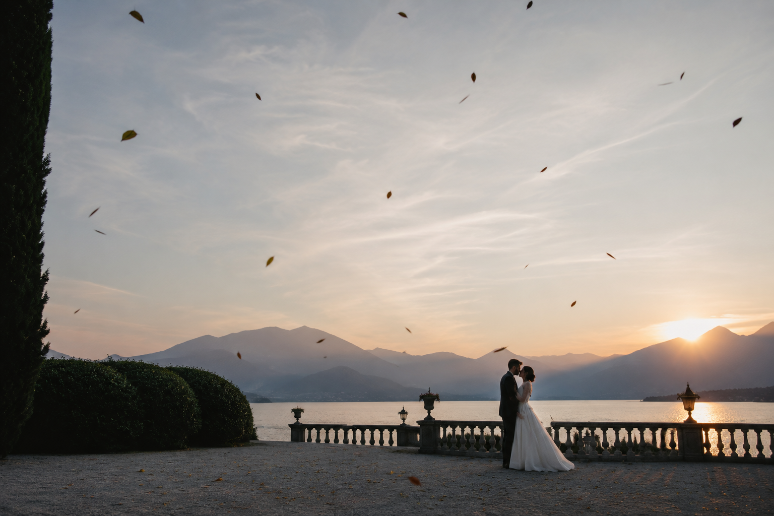 Natural destination wedding photography at a Lake Como villa, with a bride and groom embracing at sunset overlooking the lake and mountains.