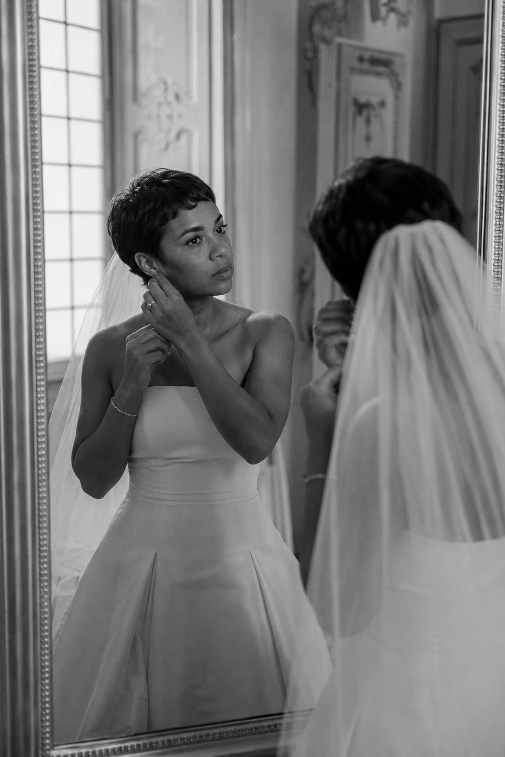 Bride adjusting her earring in front of a mirror during wedding preparations at Villa Sola Cabiati in Lake Como, photographed in a candid black and white documentary style.