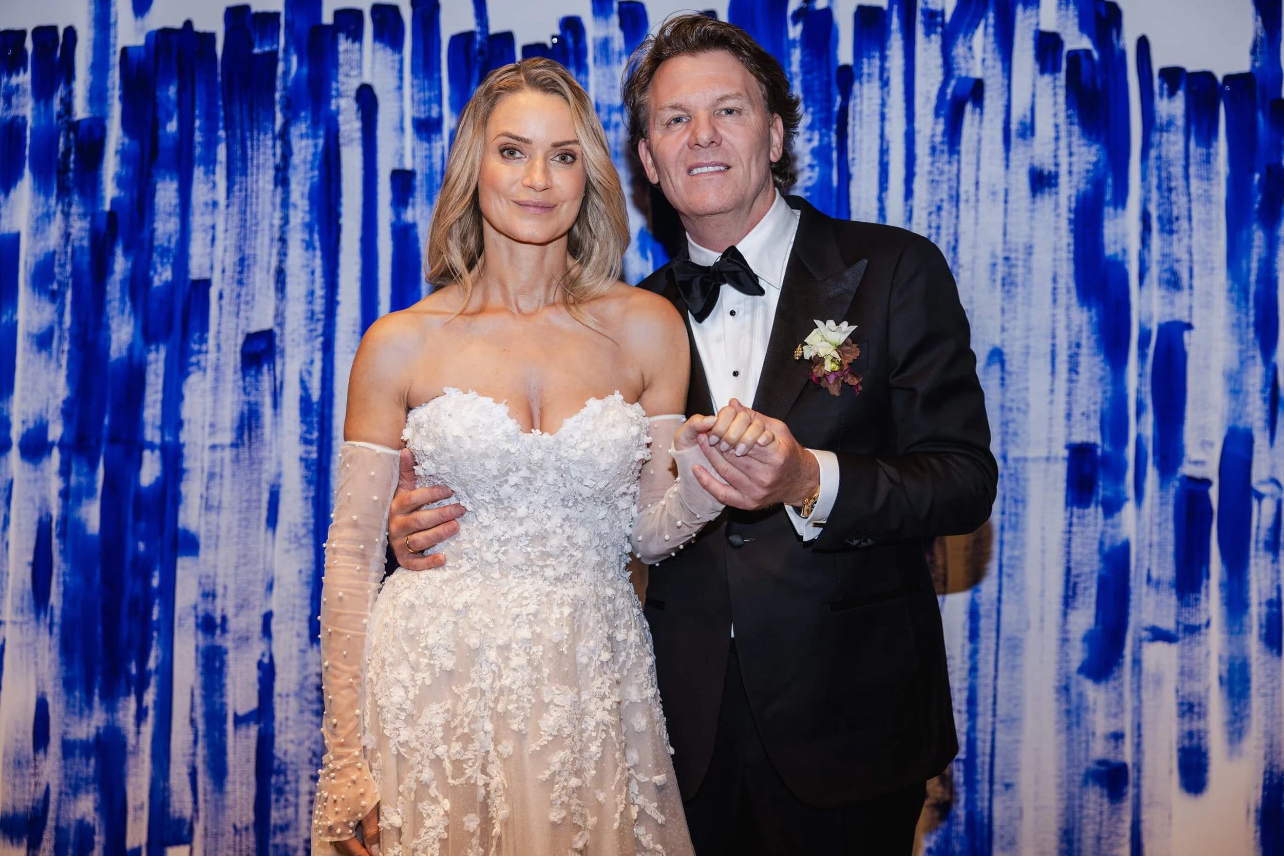 Couple standing before the collaborative blue painting created by their wedding guests