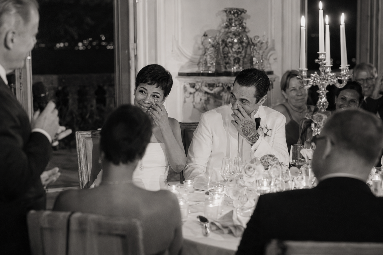 Emotional black and white dinner speech moment at Villa Sola Cabiati with couple laughing during candlelit reception on Lake Como