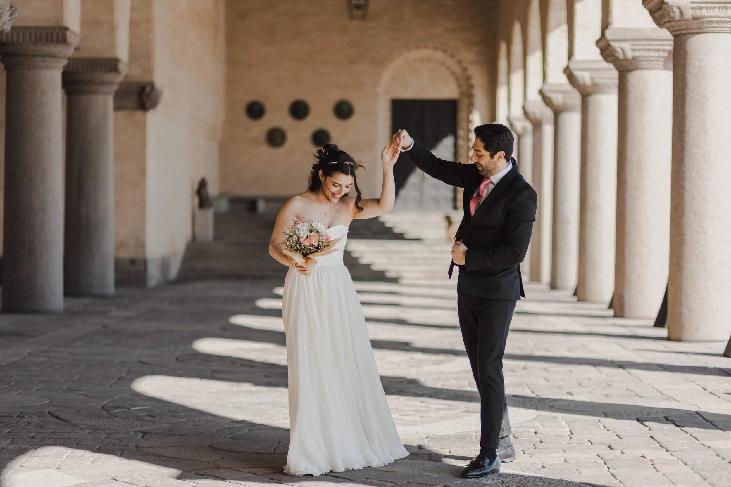 A bride and groom dancing in an outdoor corridor of Stockholm's Stadshuset with stone columns during their wedding celebration.