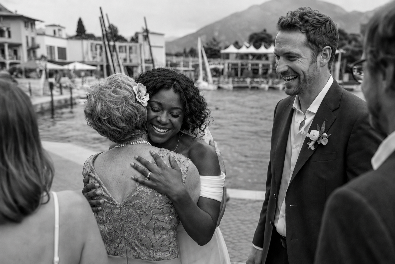 Bride hugging a family member after the ceremony in Riva del Garda while the groom smiles beside Lake Garda in a candid documentary wedding moment.