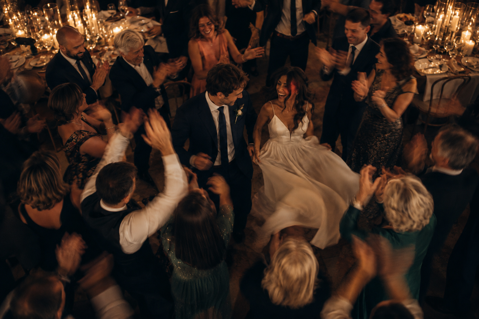 Documentary wedding dance floor moment with the bride and groom surrounded by guests, warm candlelit reception atmosphere, emotional and cinematic movement, joyful celebration, elegant evening wedding party in Italy, candid wedding photography style.