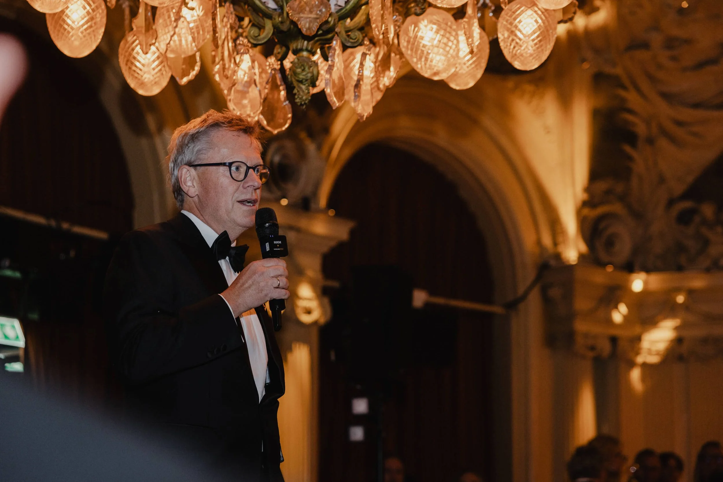 Wedding guest delivering a speech beneath a chandelier during reception at Café Opera