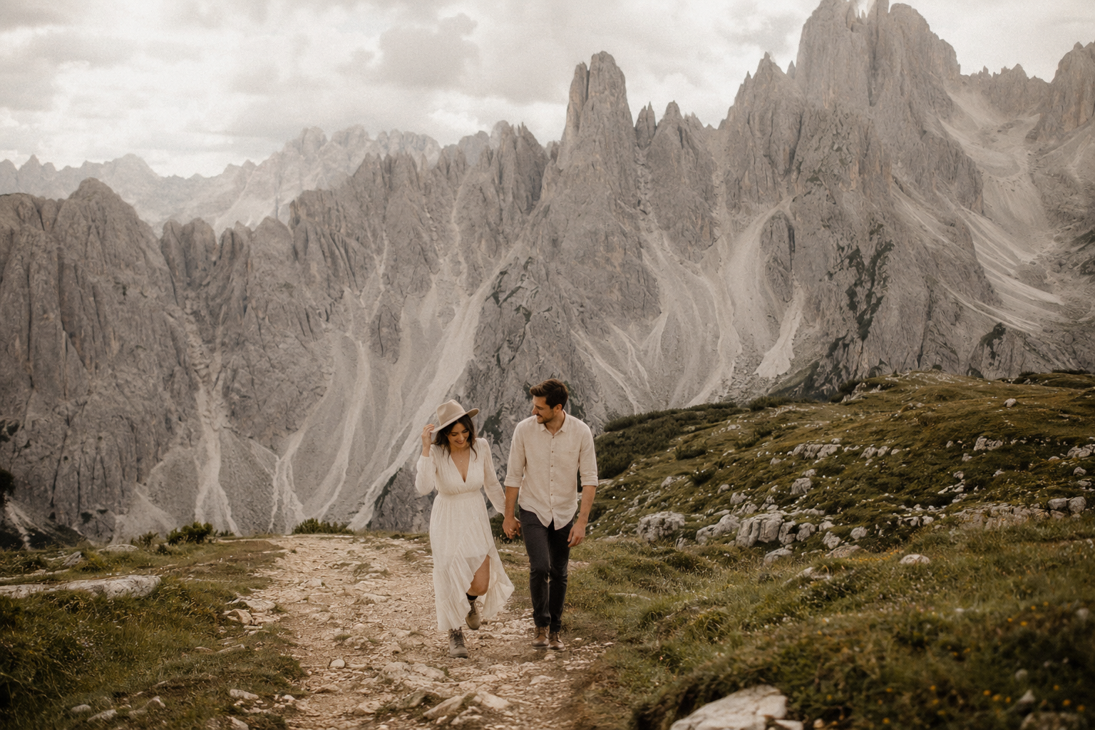Bride and groom embracing beside Lago di Carezza in the Italian Dolomites during golden hour, with emerald alpine water, dramatic mountain peaks and cinematic sunset light reflected across the lake.
