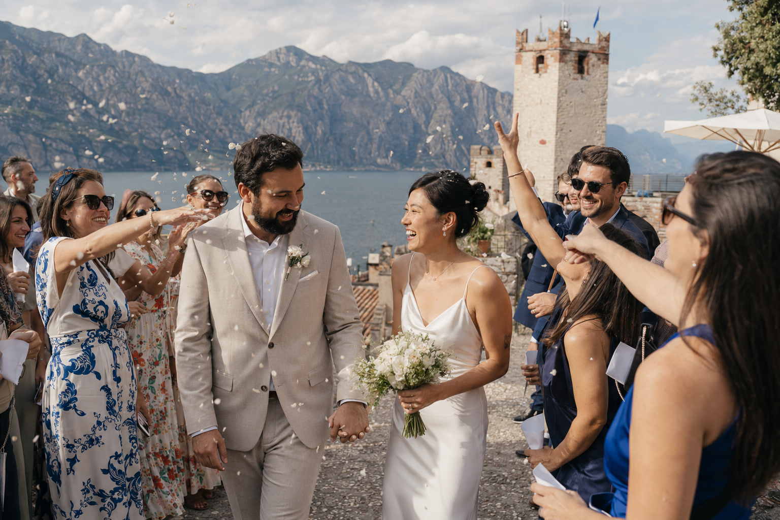 Newly married couple walking through guests after their civil wedding at Castello Scaligero di Malcesine with Lake Garda and the castle tower in the background.