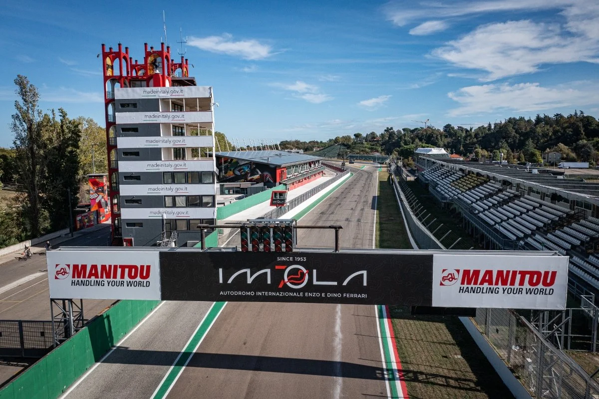 View of the Autodromo Internazionale Enzo e Dino Ferrari race track, with empty racing track, grandstands, and a control tower, under a partly cloudy sky.