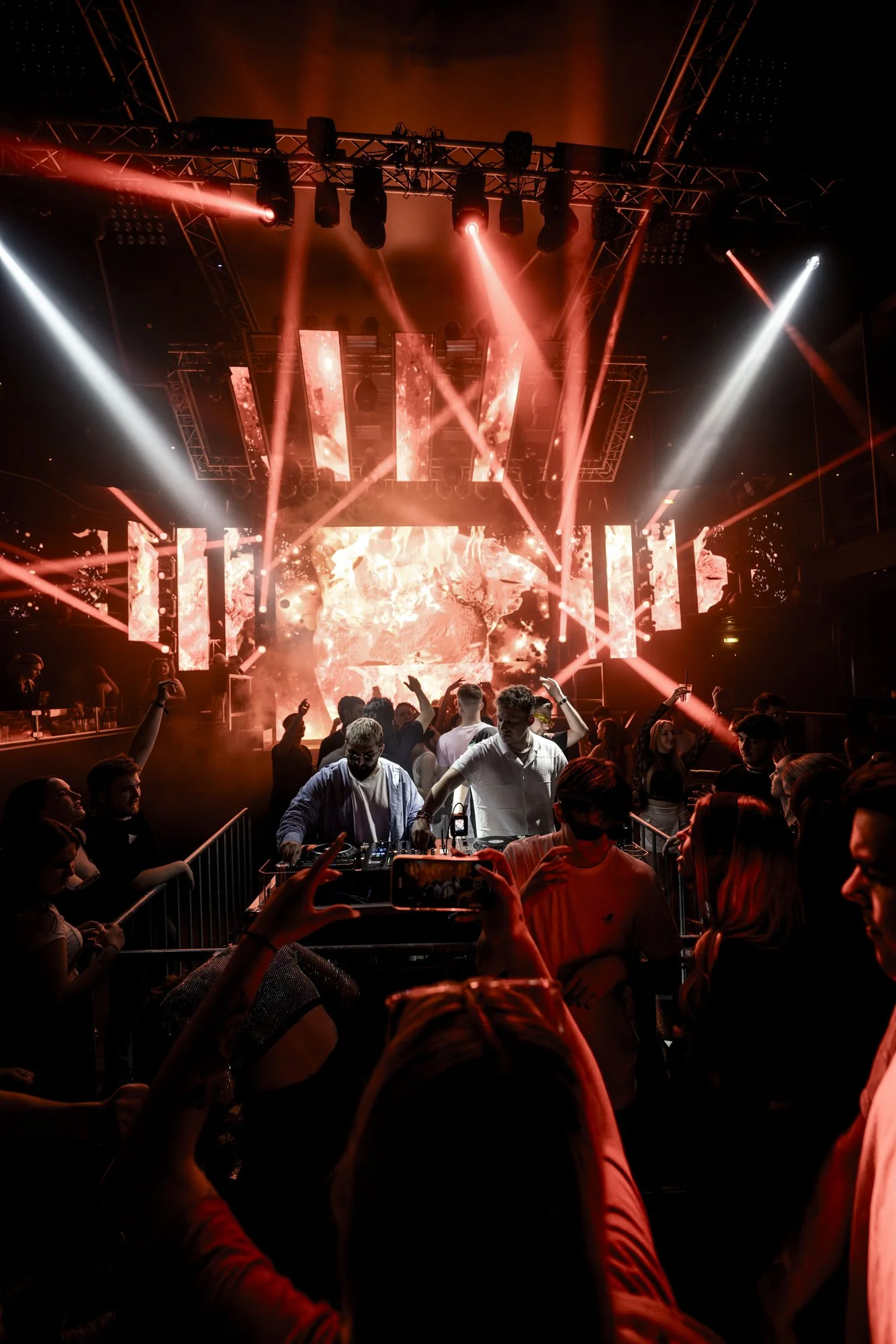 Menschen tanzen und feiern in einem Club mit einer bunten Lichtshow auf einer Bühne.