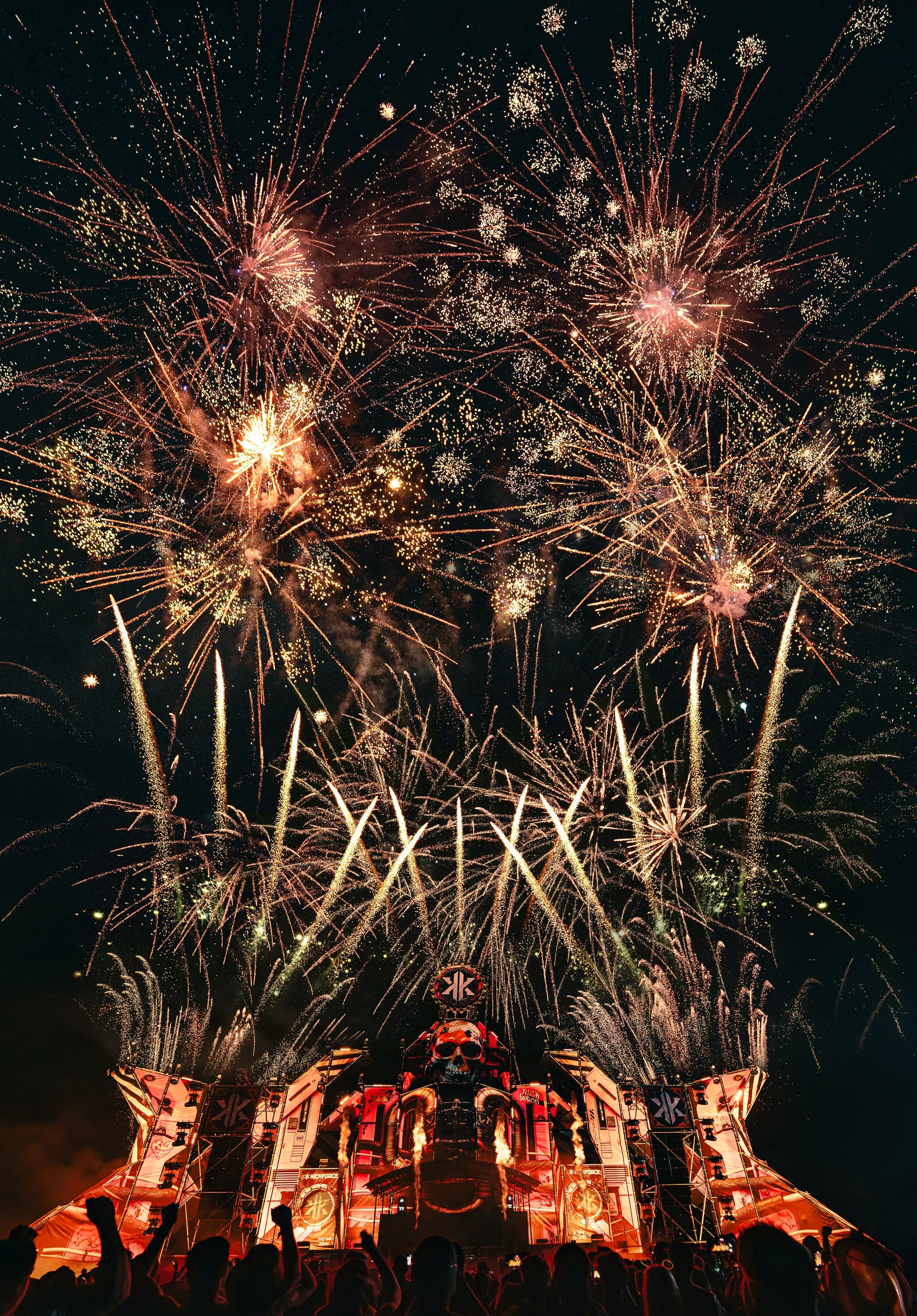 Feuerwerk erleuchtet den Nachthimmel über einer Musikfestival-Bühne mit Skull-Design, während eine Menschenmenge zuschaut.