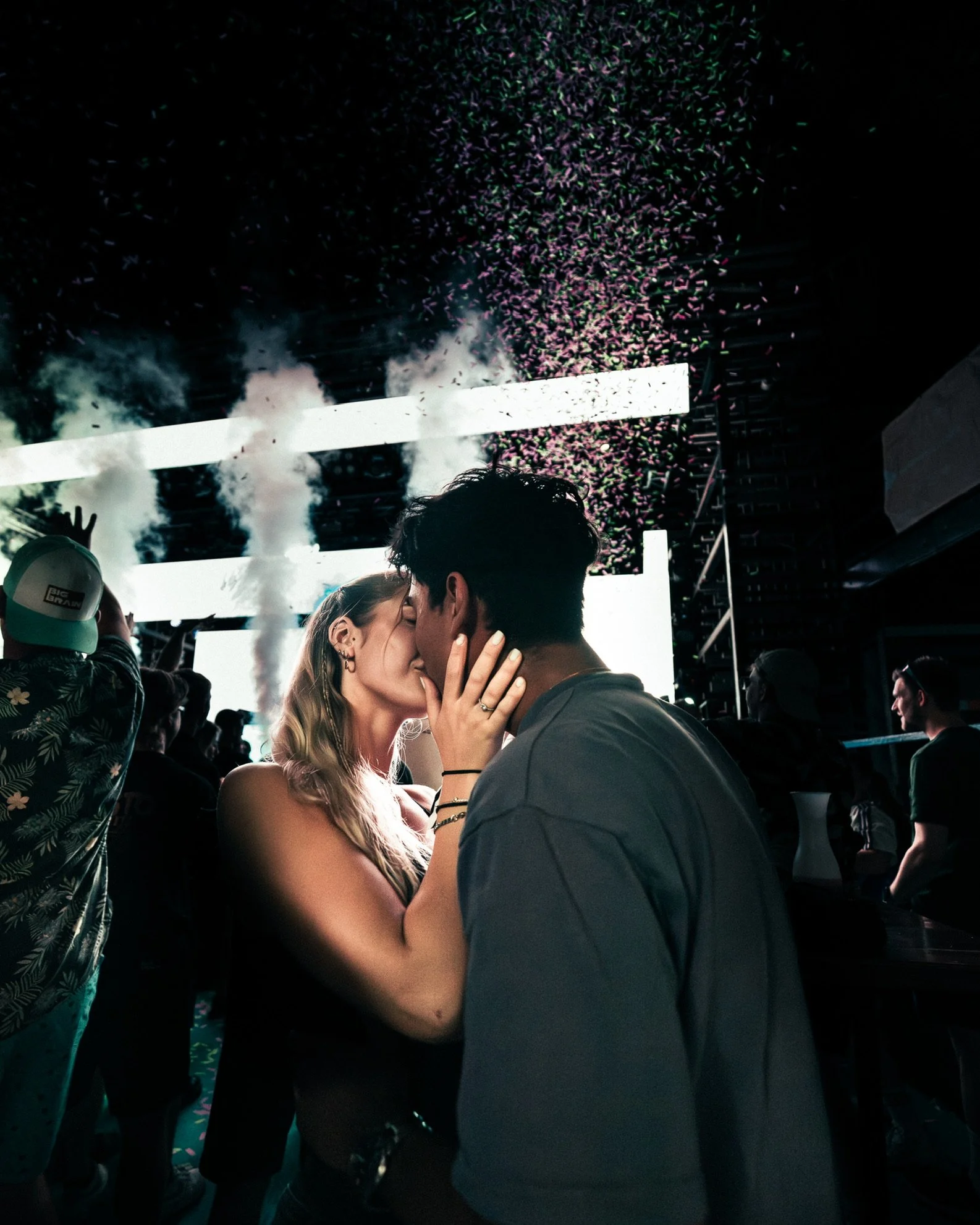 Ein Paar küsst sich auf einer Party mit Konfetti und Nebel im Hintergrund.