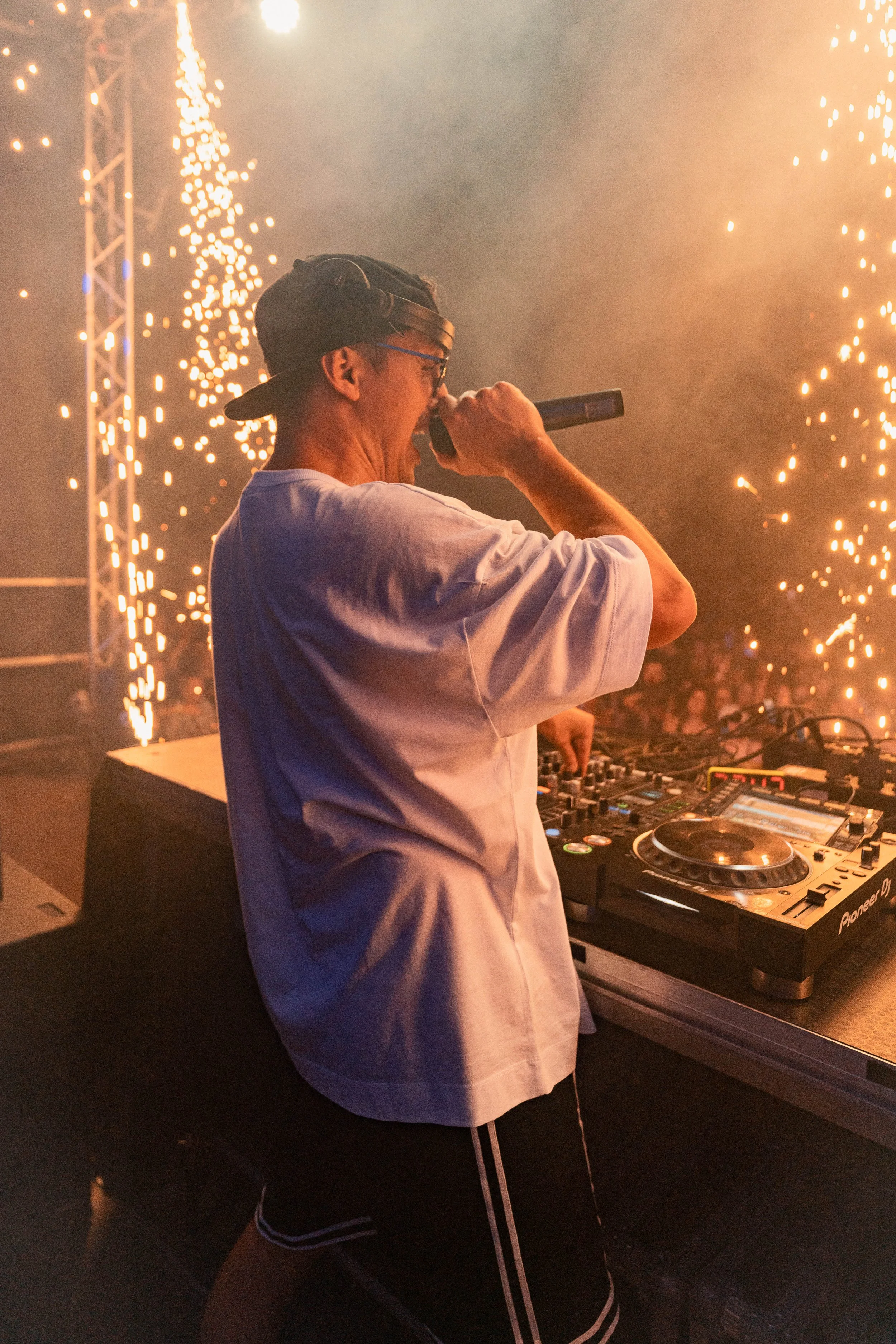 Ein DJ performt auf einer Party mit Feuerwerk und Lichteffekten im Hintergrund.