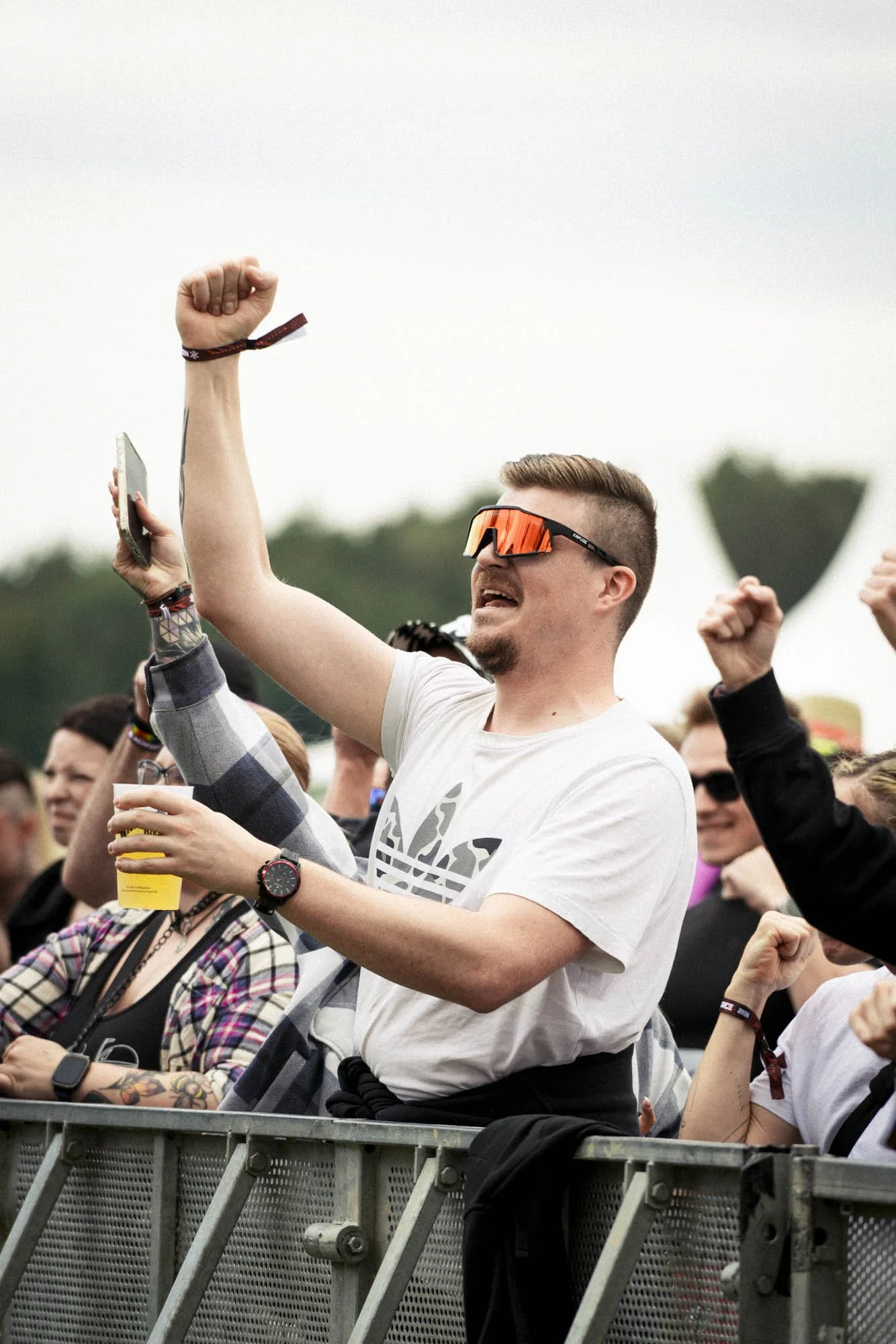 Junge Männer und Frauen beim Konzert, einer hebt die Faust in die Luft, einer trägt orange Sonnenbrille.