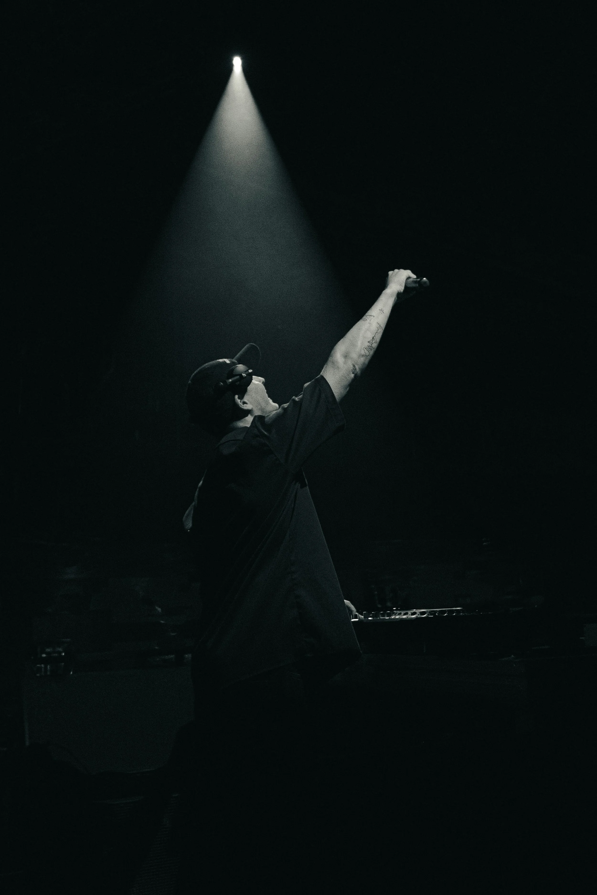 Ein DJ mit Kopfhörern hinter einem Mischpult, der die Hand in die Luft hebt, beleuchtet von einem Scheinwerfer im Dunkeln.