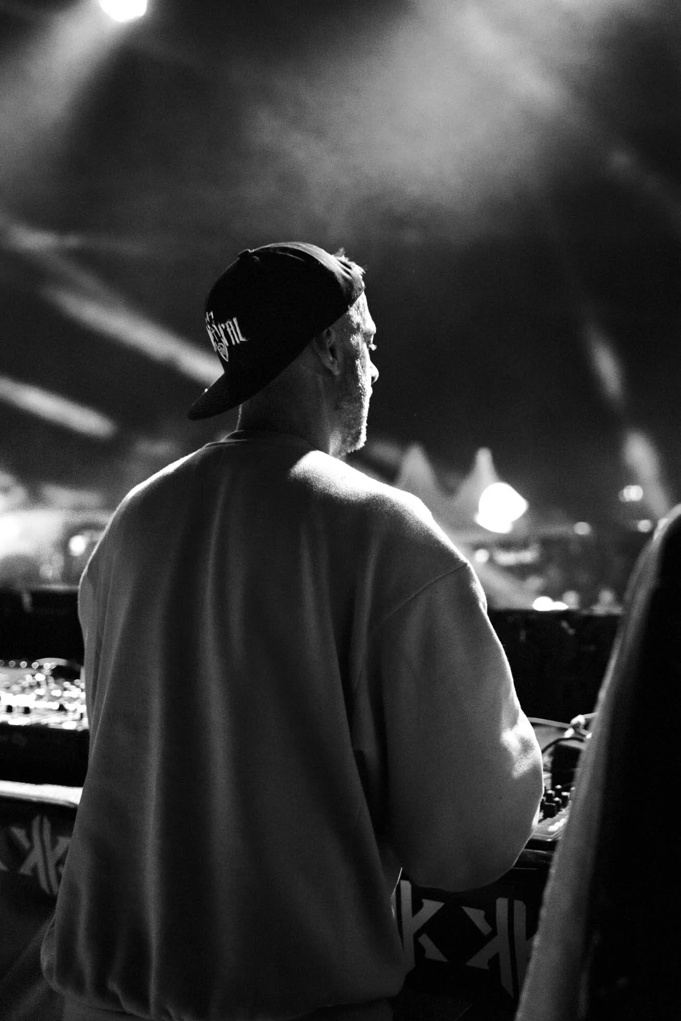 Schwarz-weiß-Foto eines DJs mit Kappe, der an Turntables in einem dunklen Club auflegt.