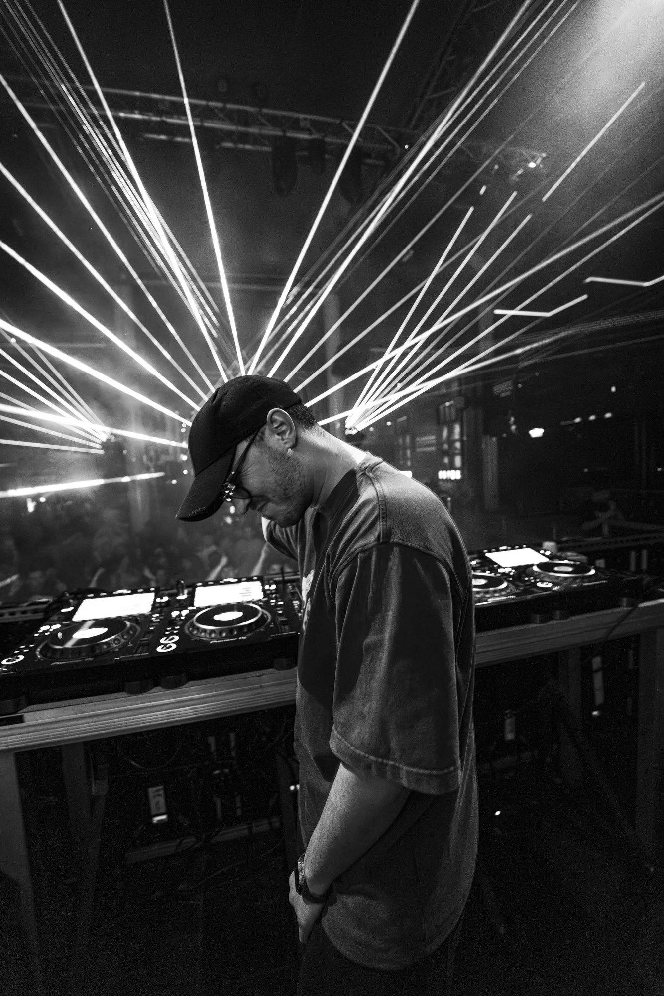 Ein DJ steht an einem Mischpult in einem Nachtclub mit Lichter- und Lasereffekten im Hintergrund.