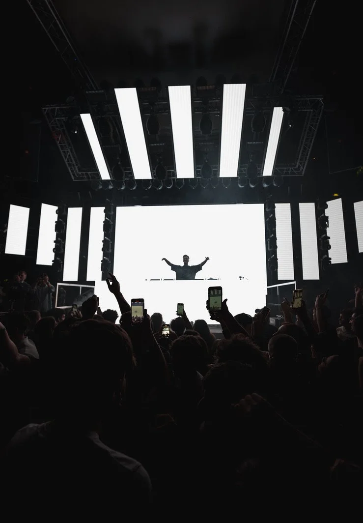 DJ auf Bühne während eines Konzerts mit Lichtshow, Publikum mit Smartphones