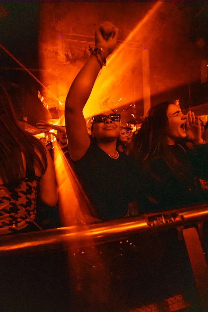 Menschen feiern bei einem Konzert, viele sind begeistert, mit orangefarbenen Lichteffekten im Hintergrund.