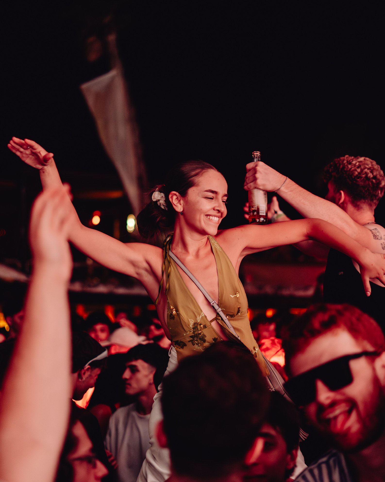 Freudige junge Frau tanzt auf einer Party im Dunkeln, umgeben von anderen feiernden Menschen.