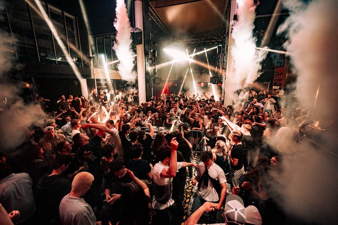 Menschen tanzen in einer dunkel beleuchteten Diskothek mit Rauch und Lichteffekten.