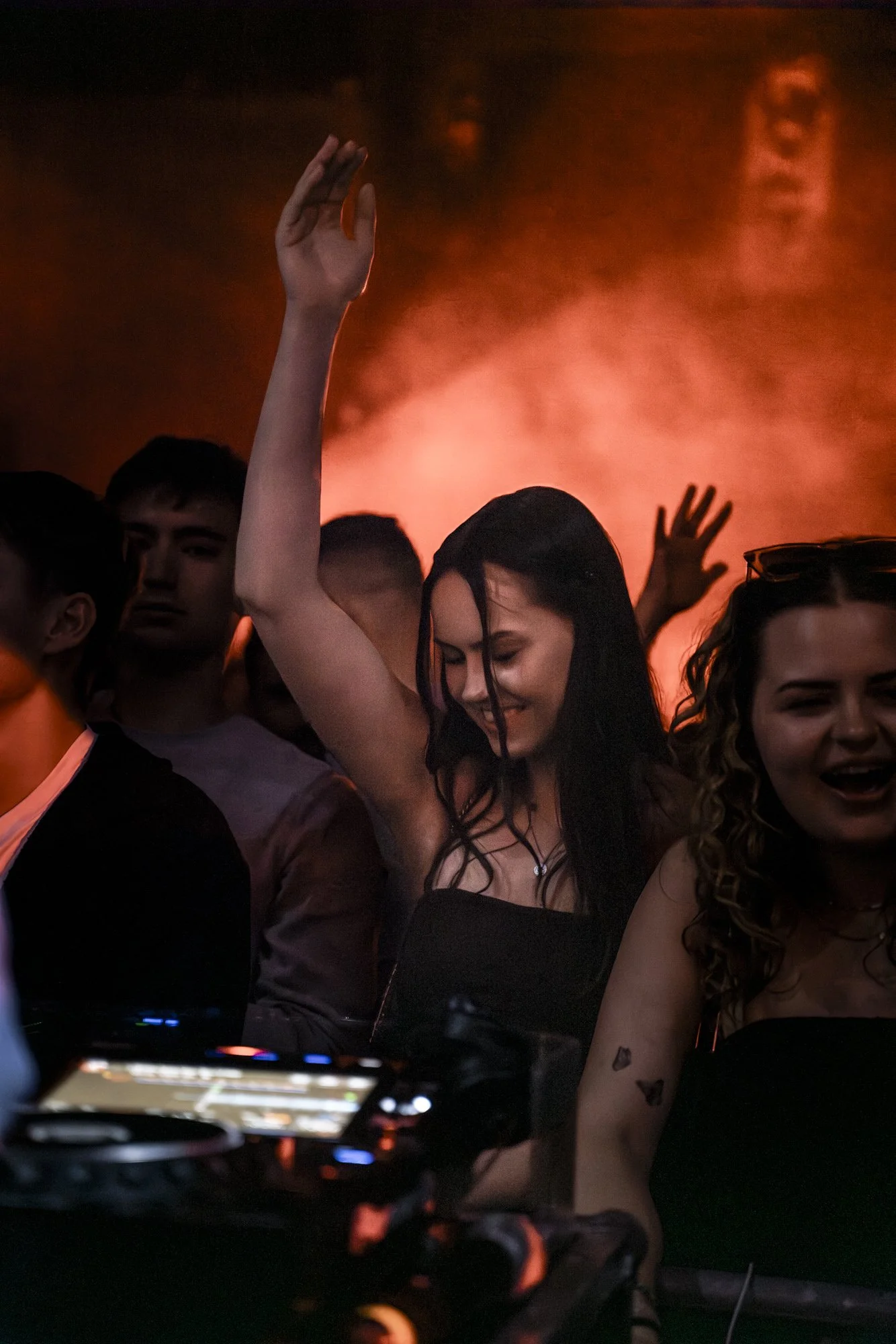 Frauen tanzen und feiern bei einer Party mit rotem Licht im Hintergrund.