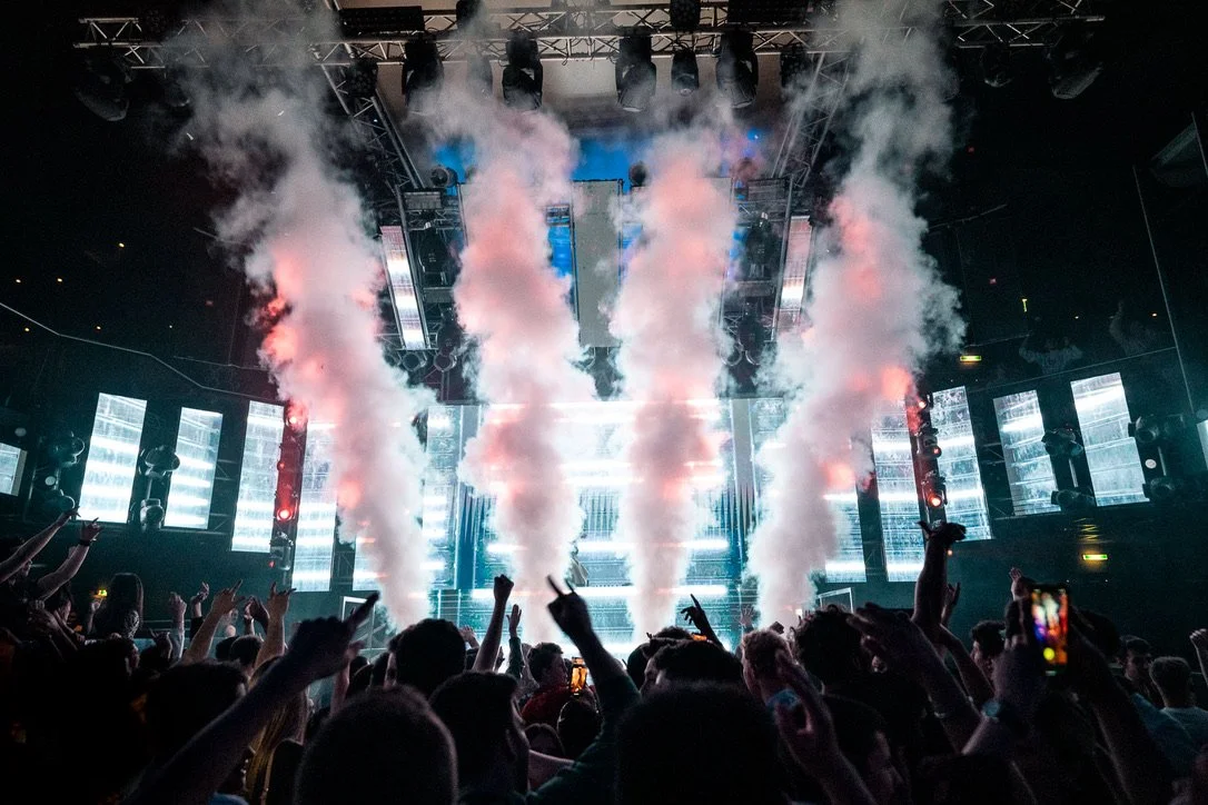 Menschenmenge auf einem Konzert mit Rauch- und Lichteffekten auf der Bühne.