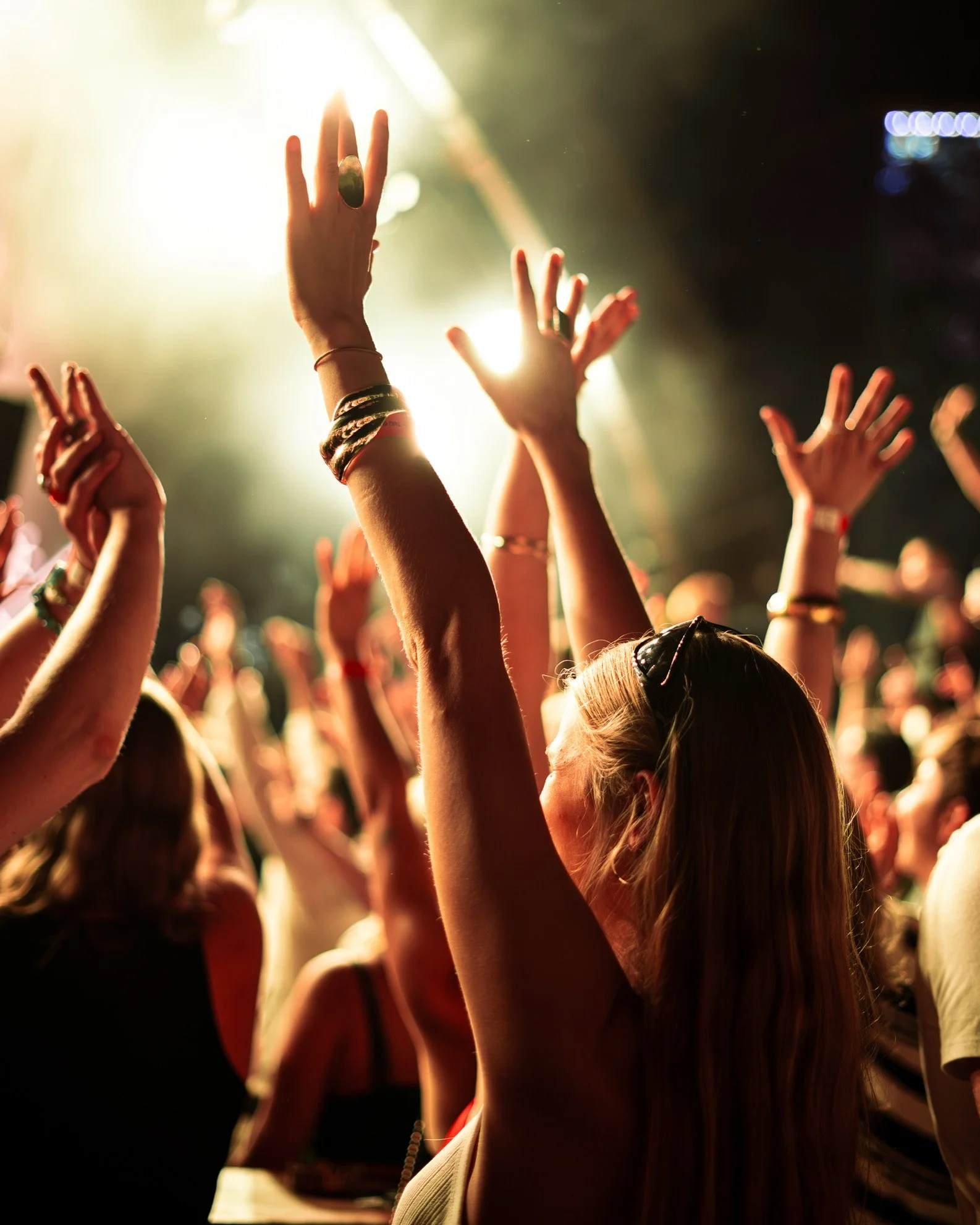 Menschen tanzen und heben die Arme bei einem Konzert unter buntem Scheinwerferlicht.