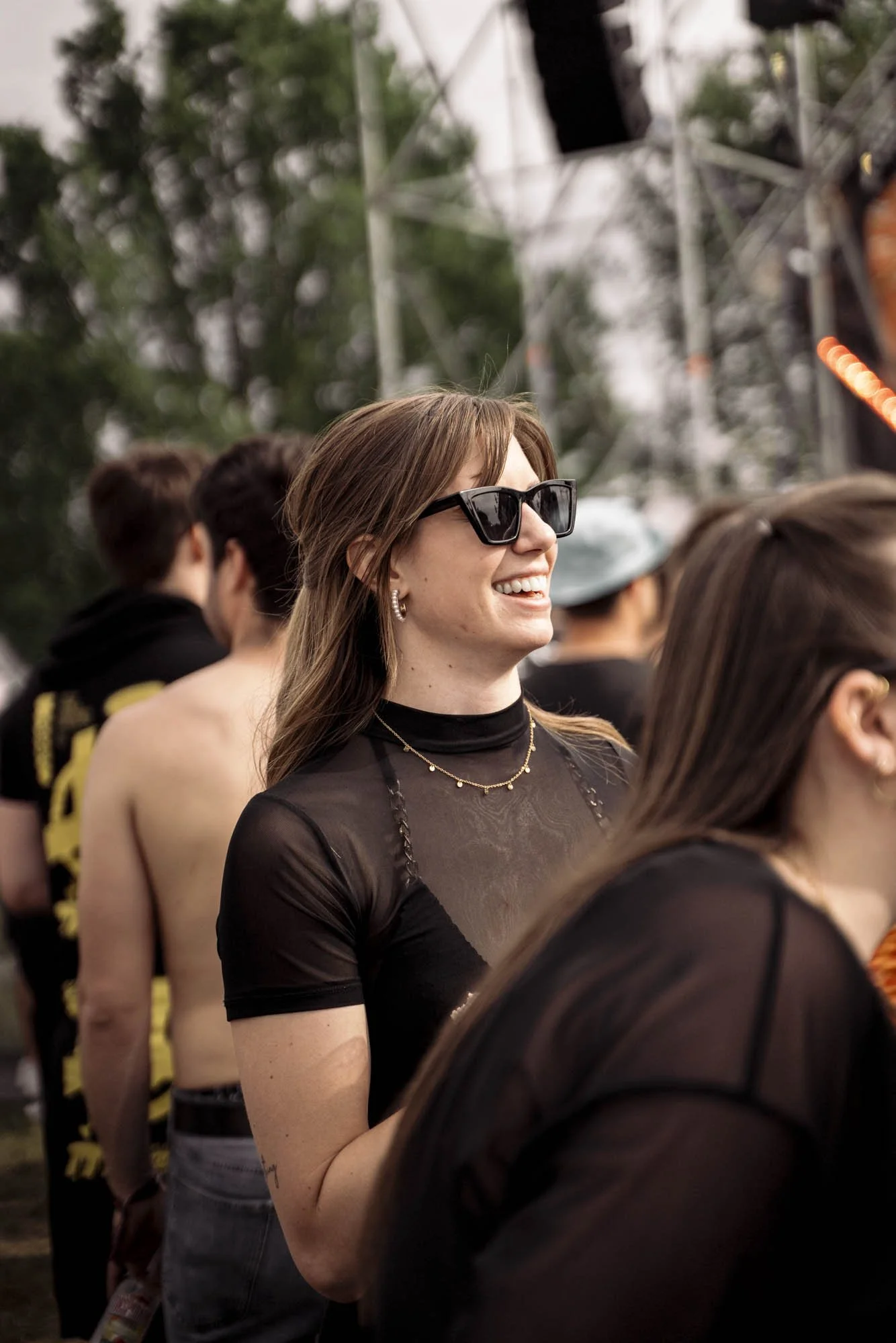 Menschen auf einem Konzert, lachende Frau mit Sonnenbrille und dunklem Top im Vordergrund.