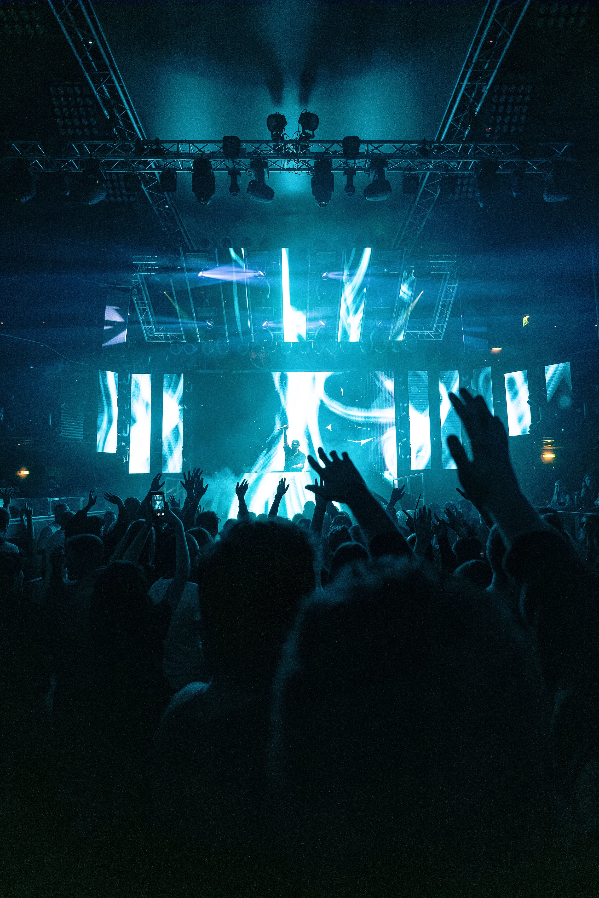 Menschenmenge beim Konzert mit Beleuchtung und DJ auf der Bühne.